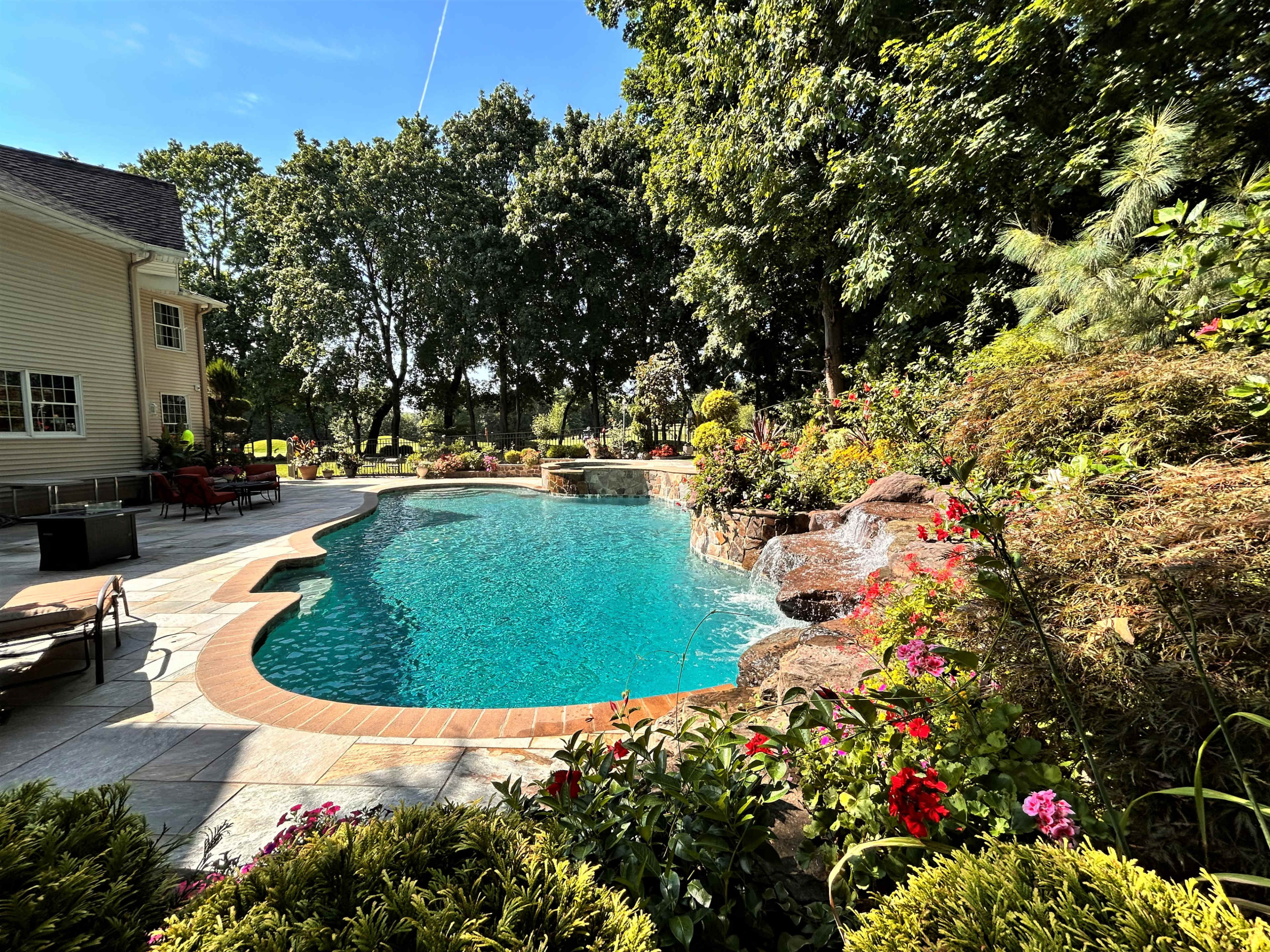 A backyard features a swimming pool surrounded by lush greenery and colorful flowers.