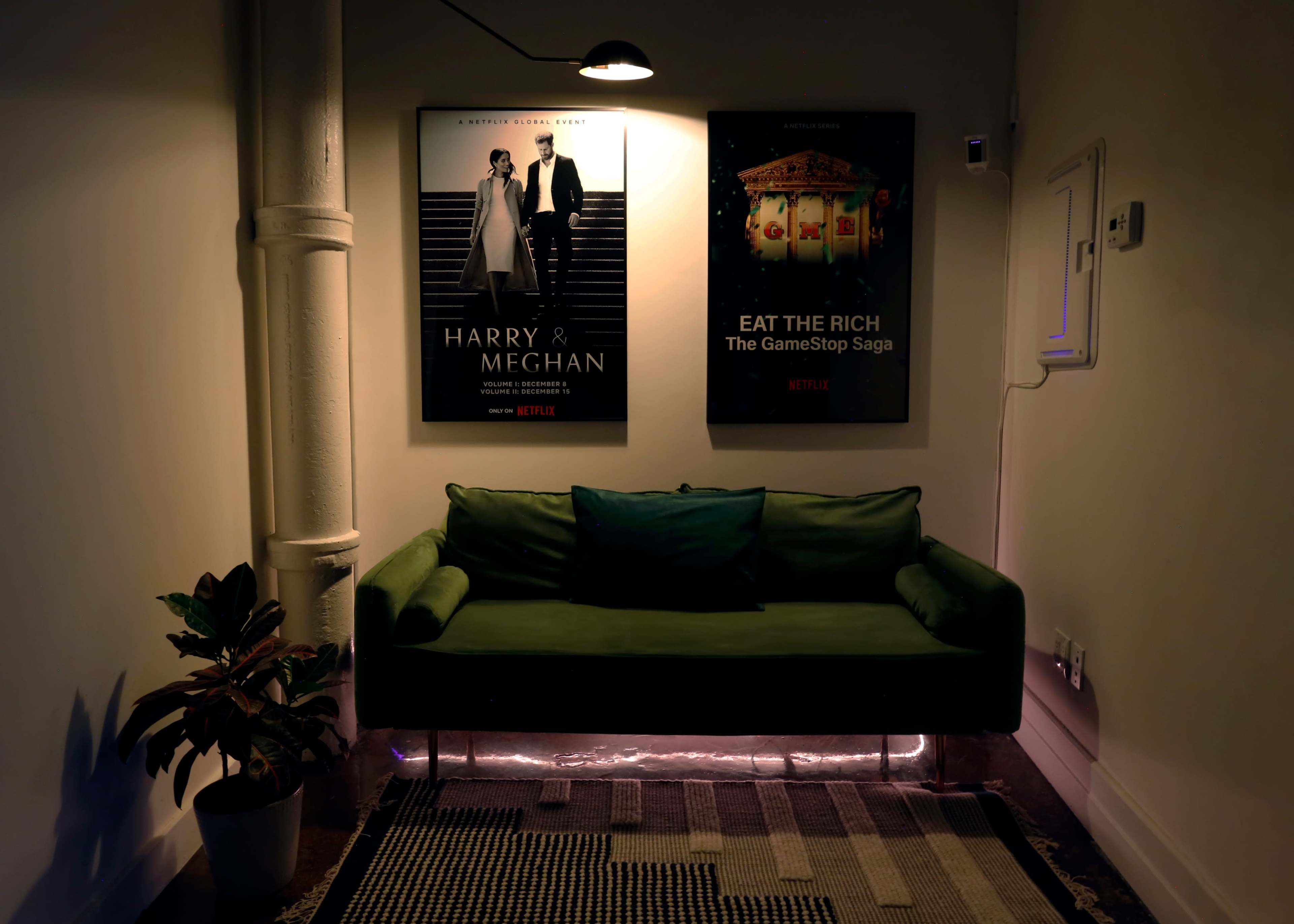A green couch is positioned against a wall featuring two movie posters, one for "Harry & Meghan" and the other for "Eat the Rich: The GameStop Saga," alongside a small potted plant.