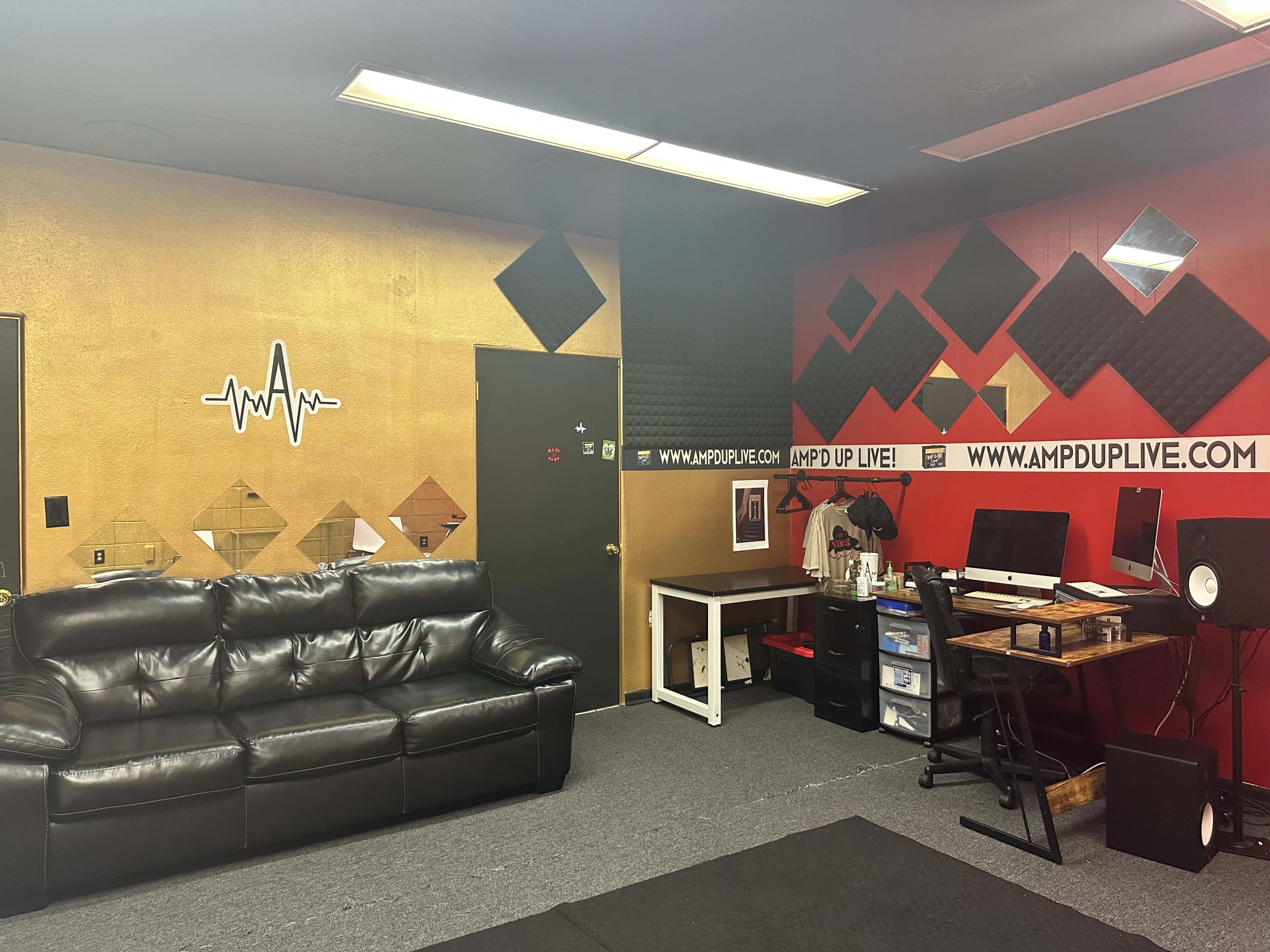 A music studio with black leather seating, soundproof walls, and a workstation equipped with computers and audio equipment.