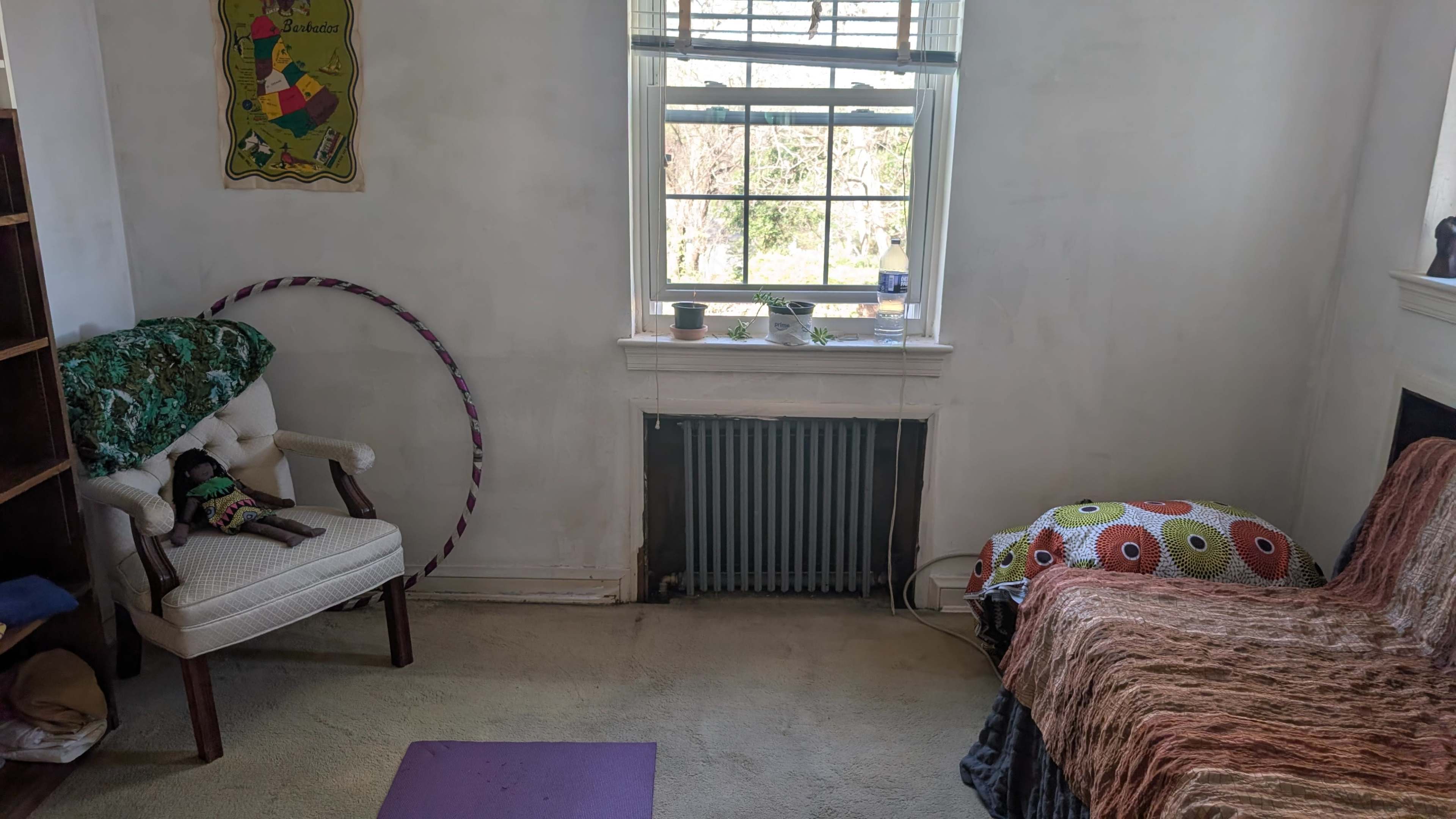 The image shows a simple room with a chair, a small bed, a hoop, a radiator, and a window letting in natural light.