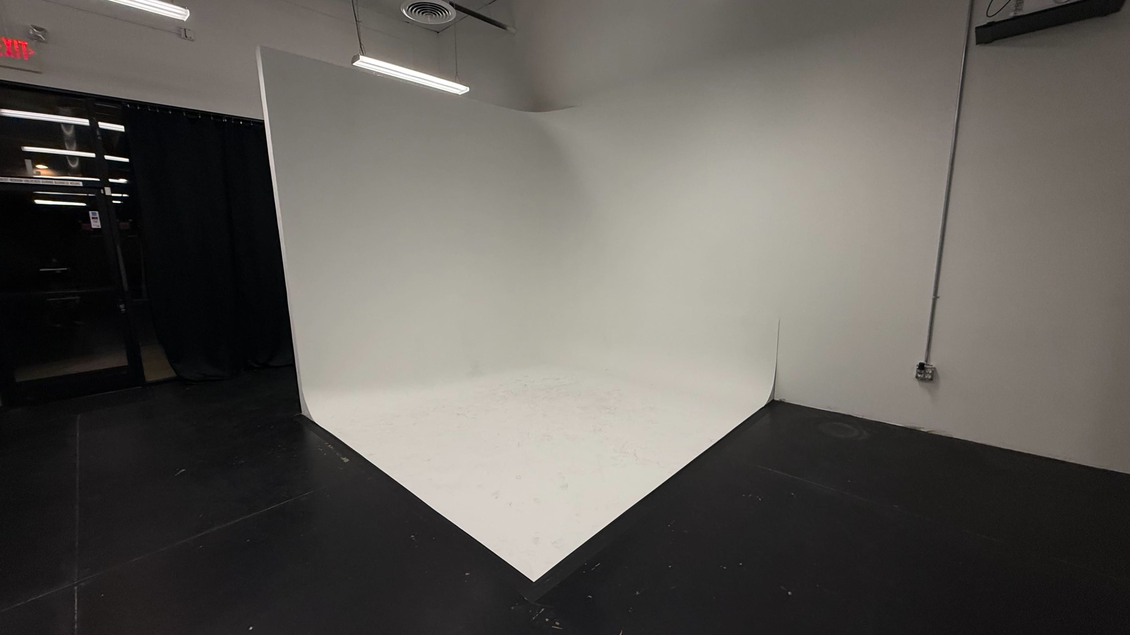 The image shows a blank studio space with a large white backdrop in a corner and black curtains on one side.