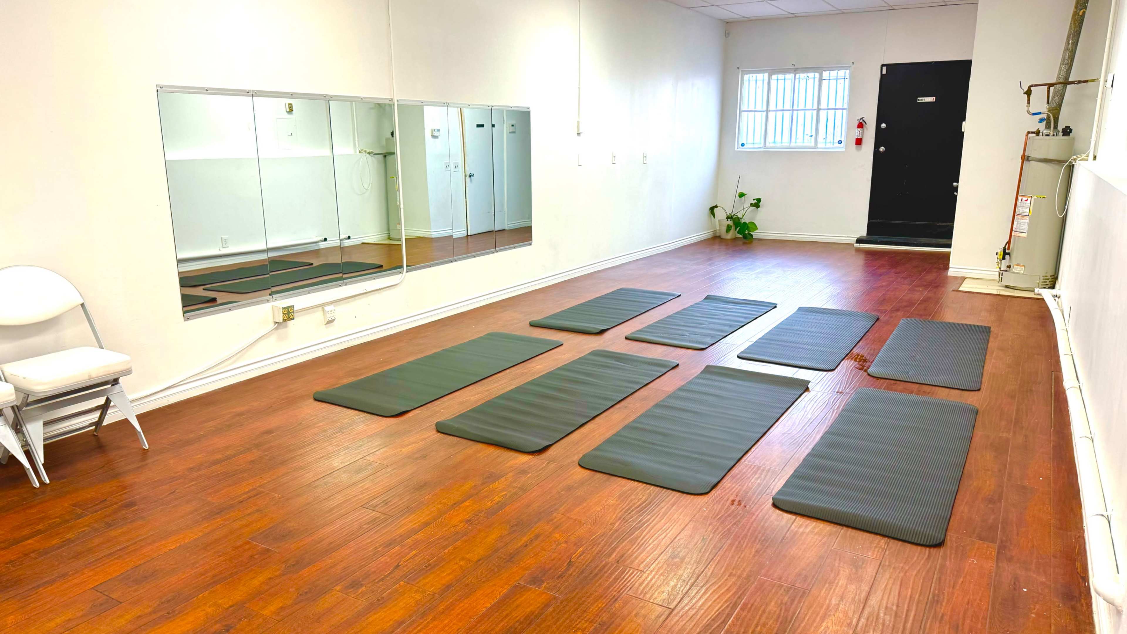 A spacious room with brown wooden floors, featuring neatly arranged exercise mats and a mirror on one wall.