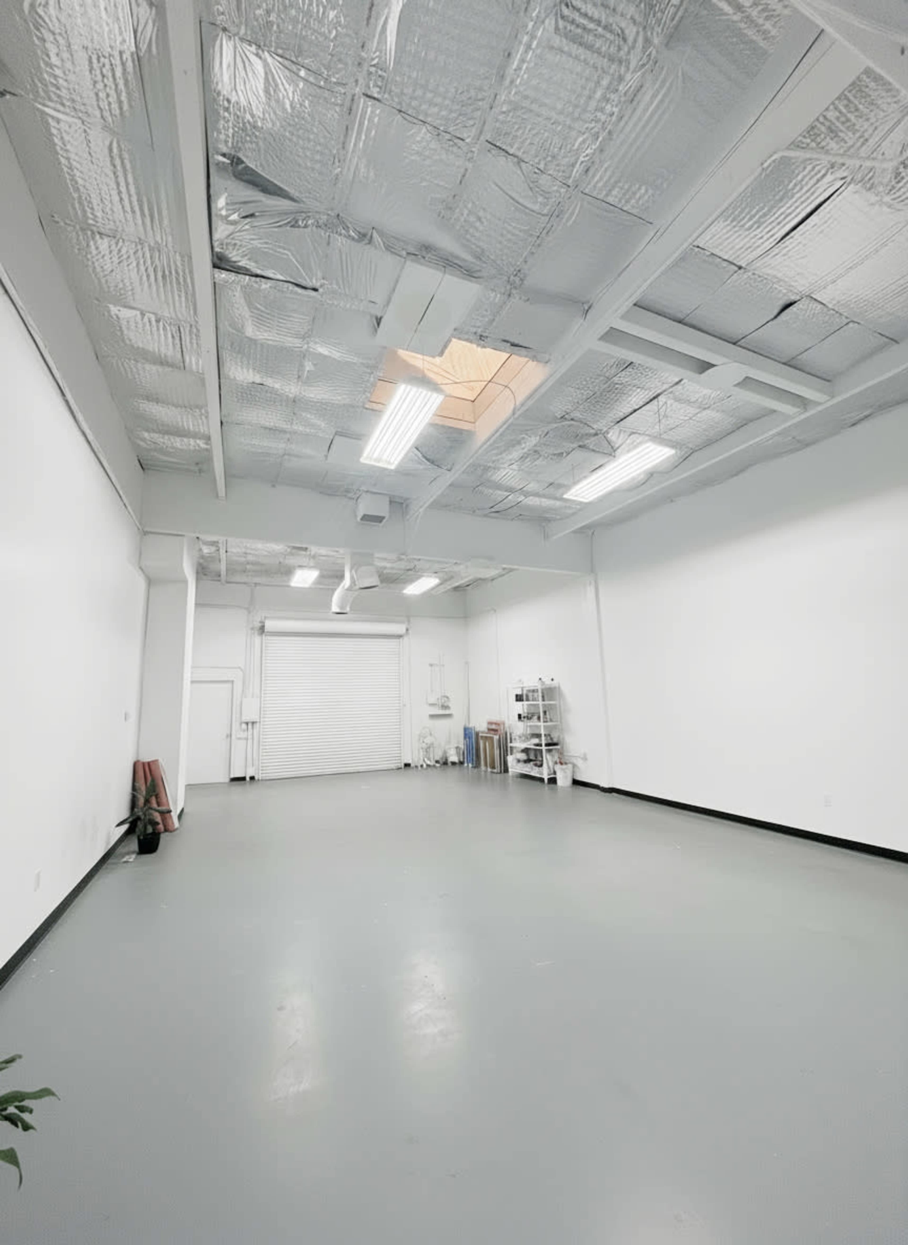 The image shows a spacious, empty room with a glossy gray floor, white walls, and a section of the ceiling that has exposed insulation.