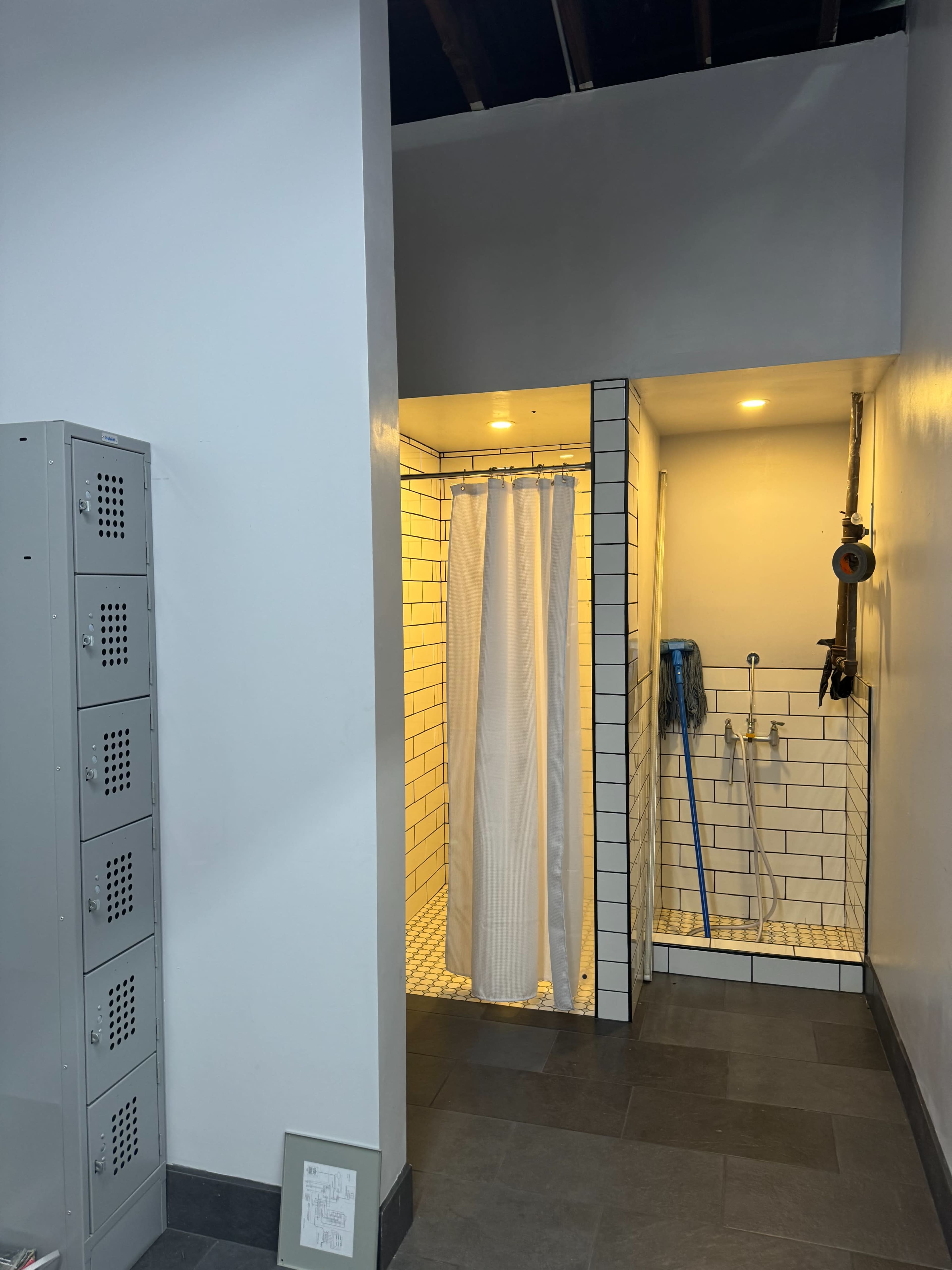 A clean bathroom area featuring a shower with a white curtain, a tiled floor, and lockers to the left.