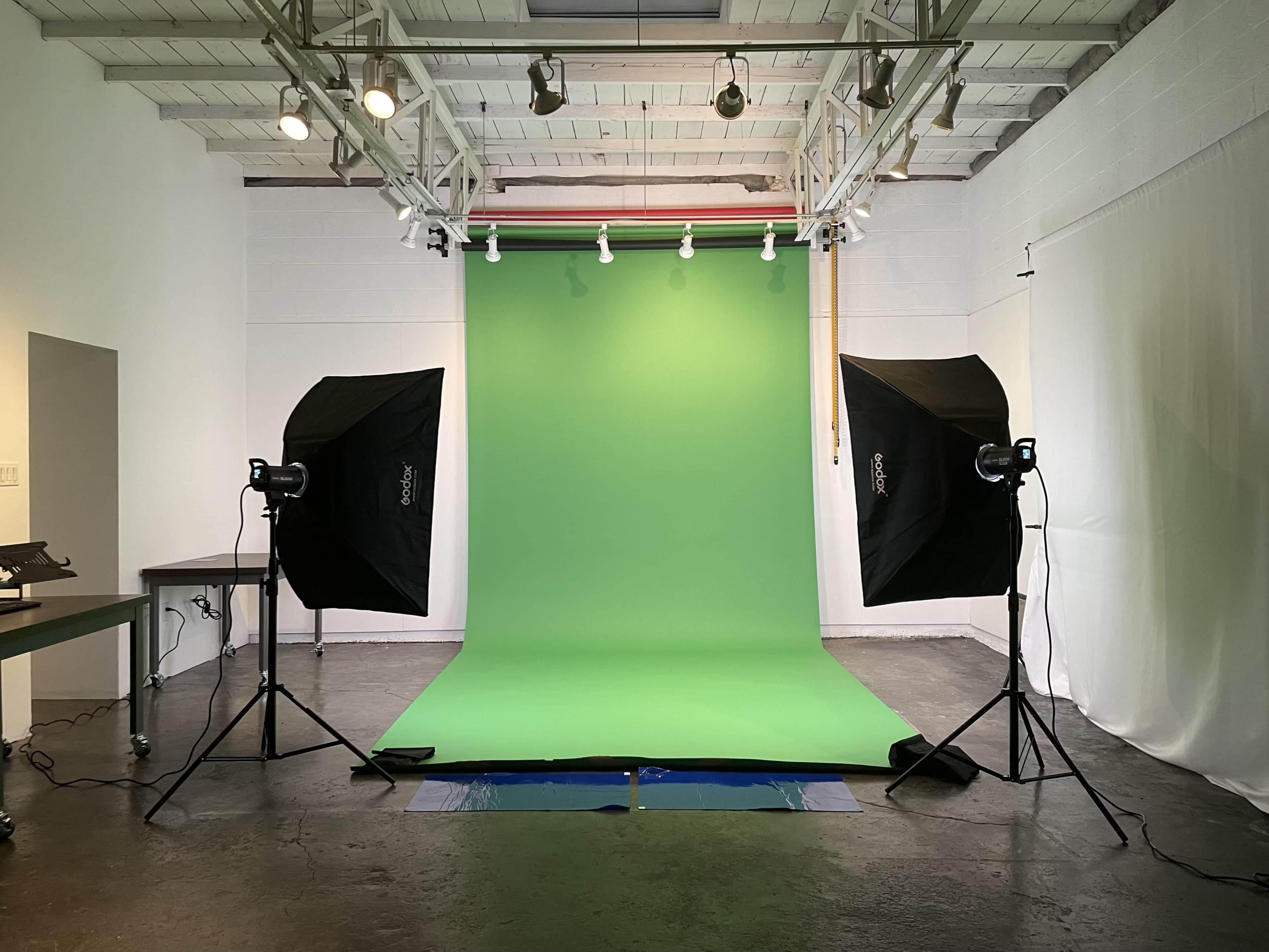A photography studio with a green backdrop and two softbox lights positioned on either side.