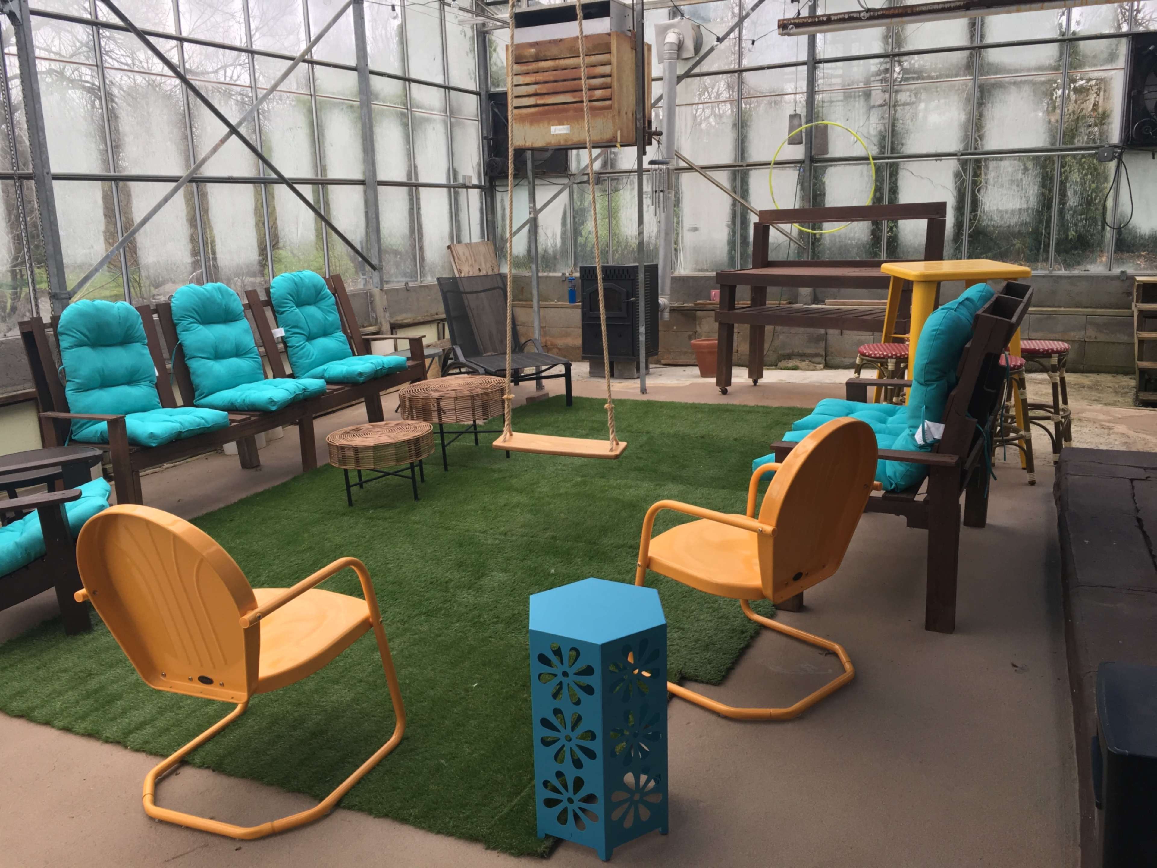 A greenhouse area furnished with bright chairs and a swing, arranged around a grassy carpet.