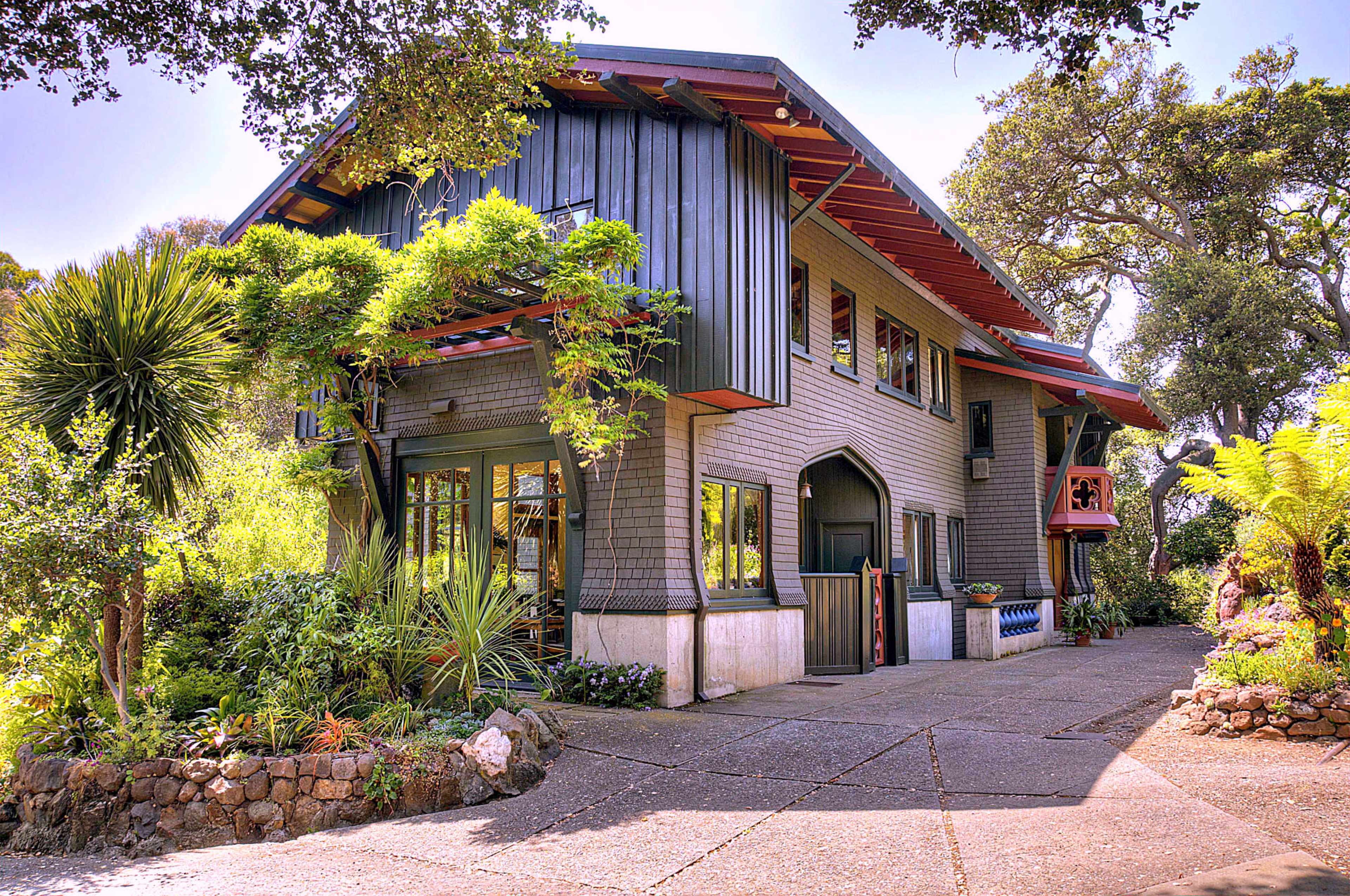 A large, intricately designed house with a mix of modern and traditional architectural elements, surrounded by lush greenery and a stone pathway.