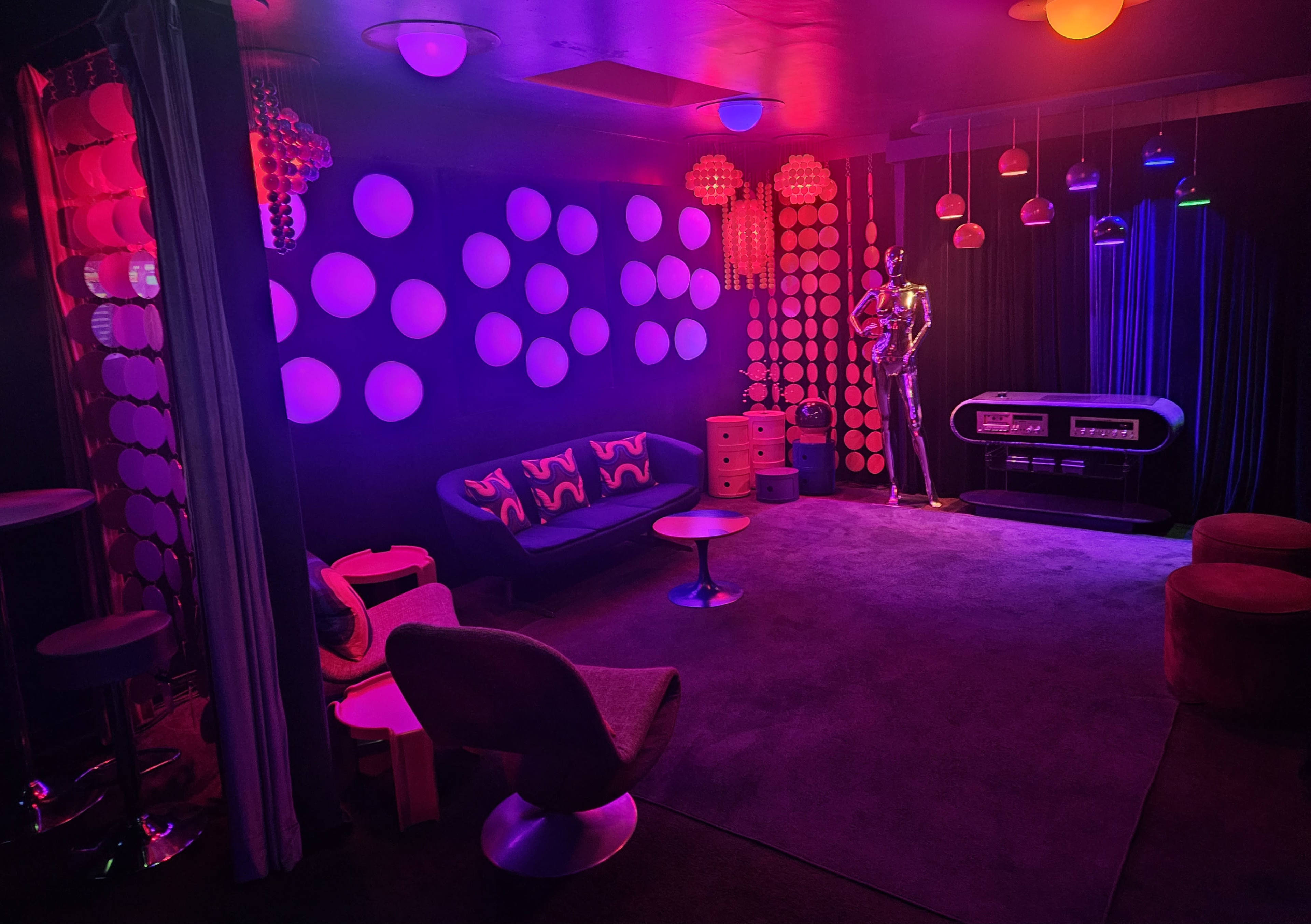 The scene features a retro-themed lounge with colorful lighting, circular wall decor, a curved sofa, and a vintage-style jukebox.