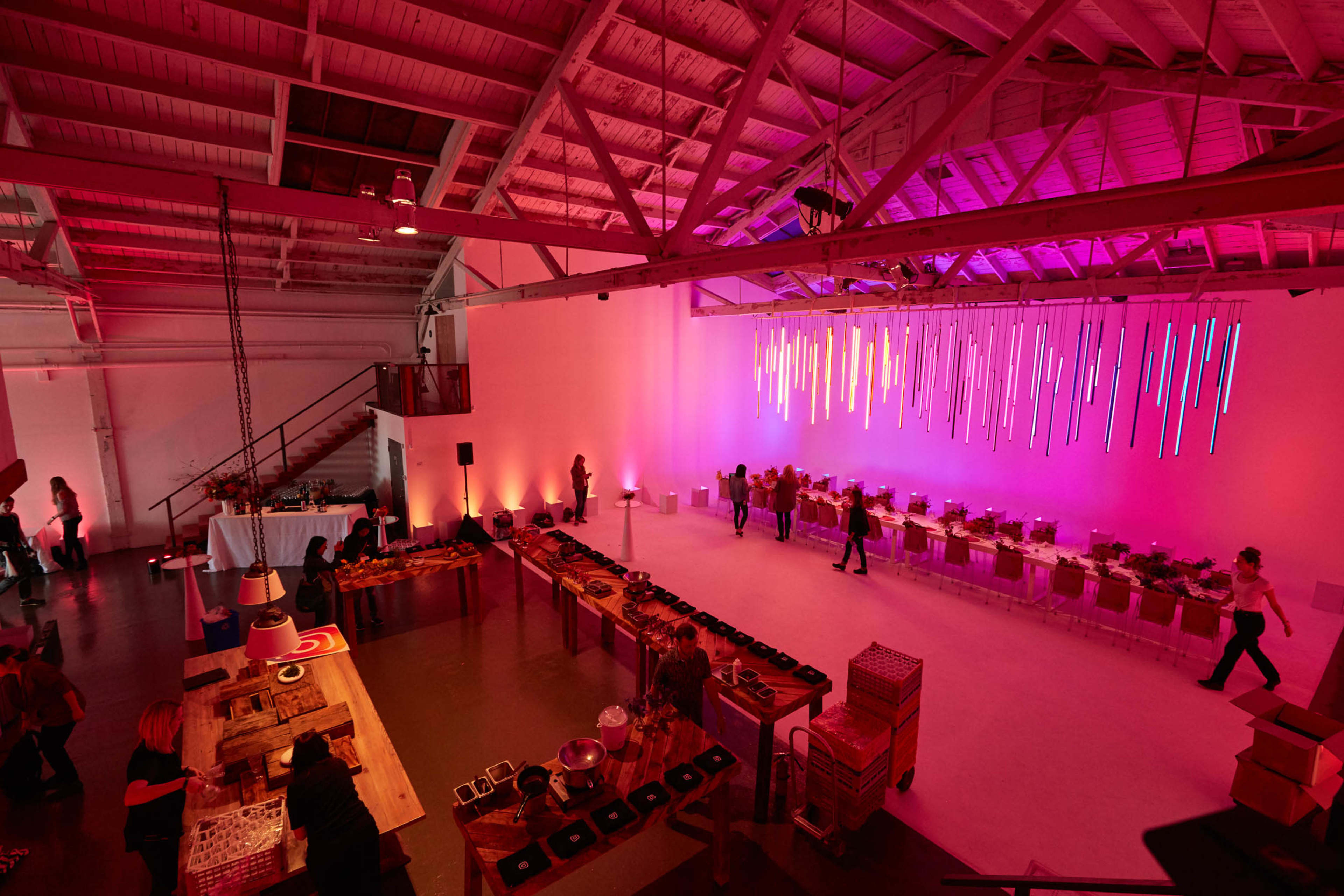 A spacious event venue features long tables set for a gathering, with colorful lights illuminating the space and a buffet area in the foreground.