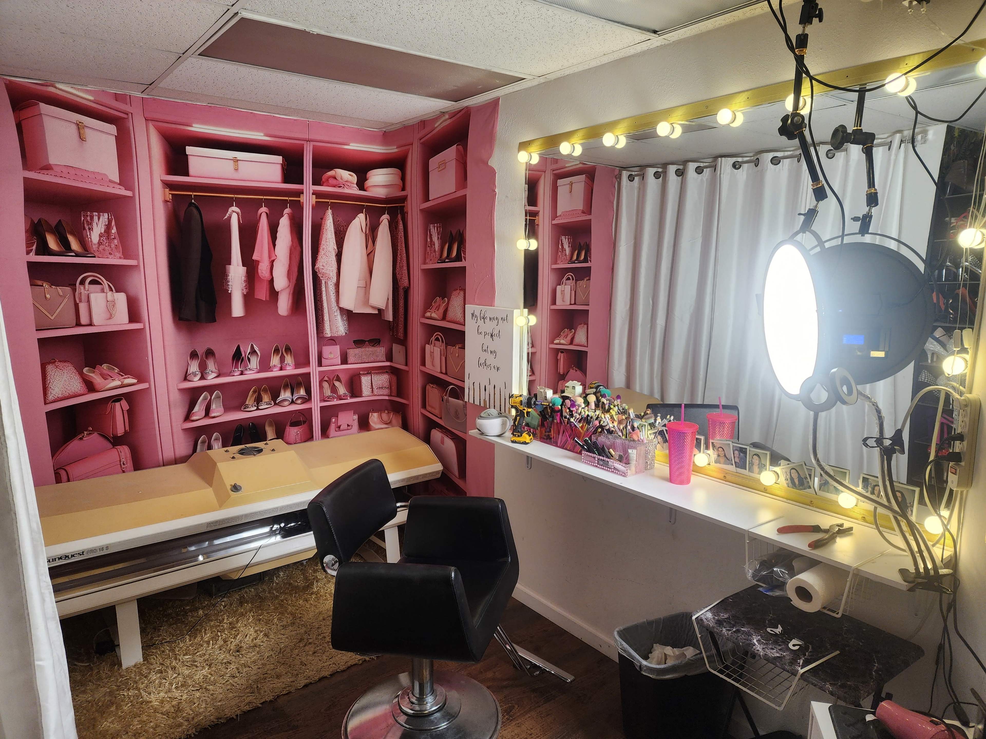 A pink-themed dressing room with organized shelves of shoes and clothing, a makeup station with lights, and a salon chair.