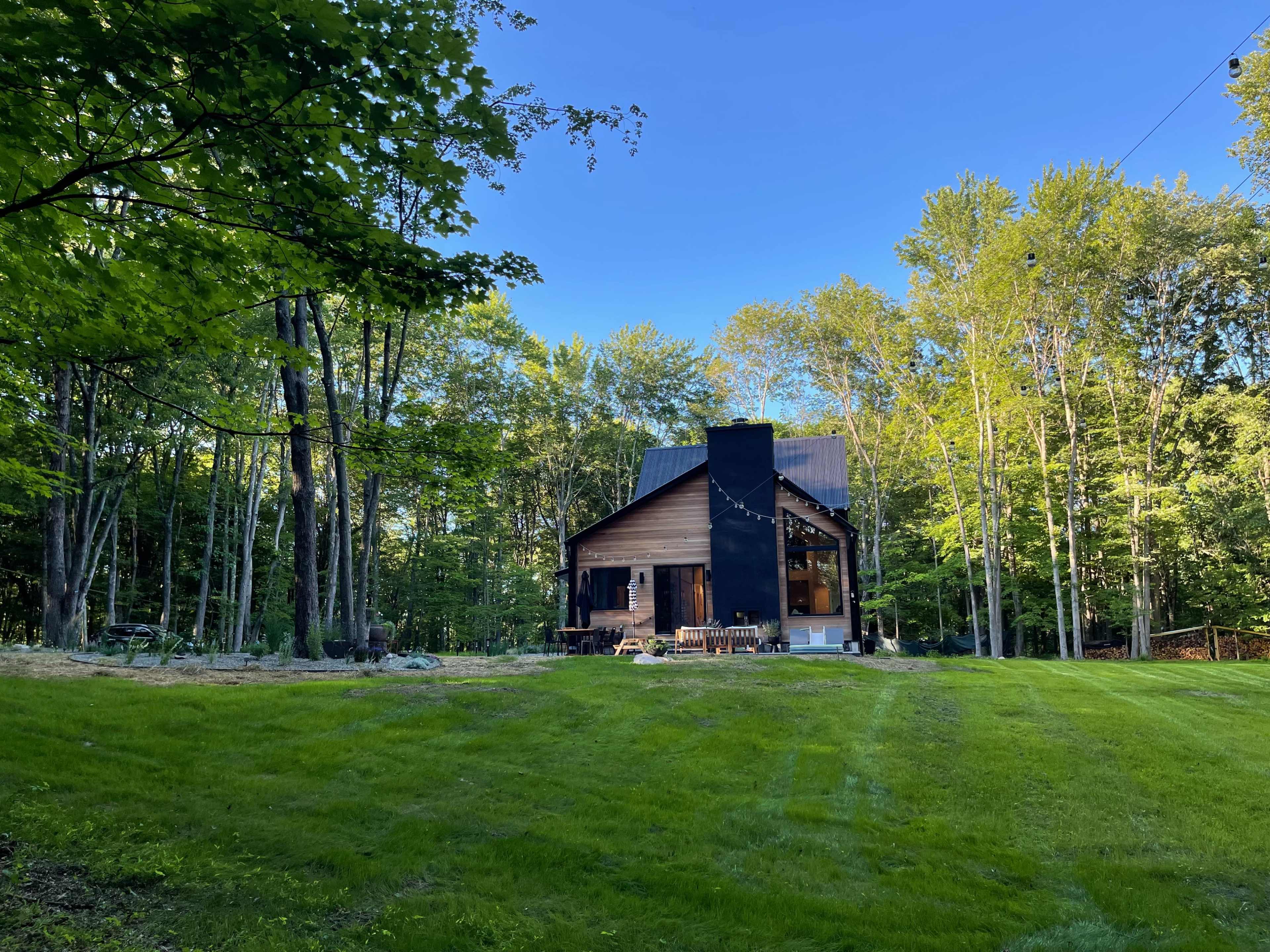 A modern house with a black chimney is surrounded by lush green grass and trees under a clear blue sky.