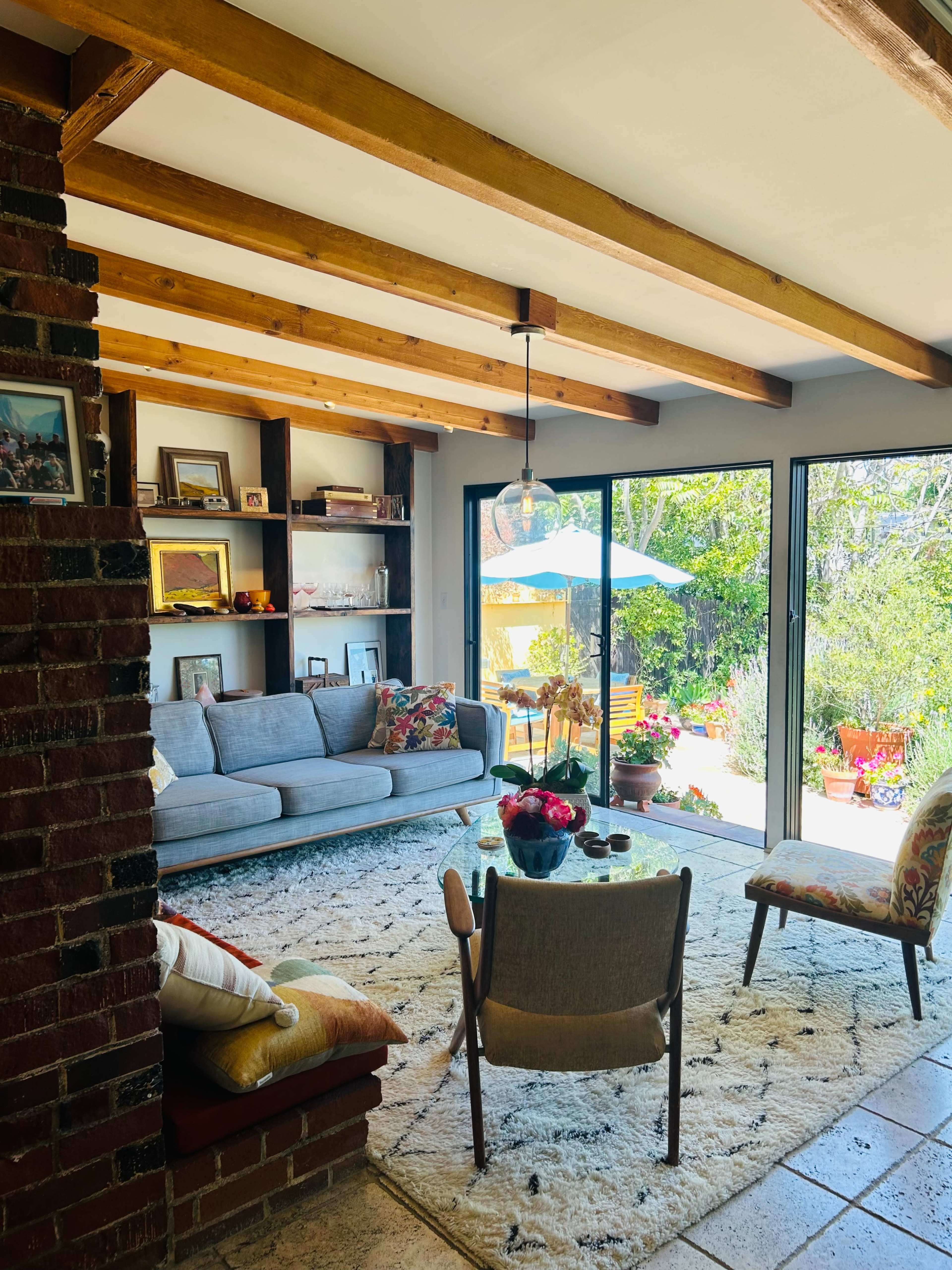 A modern living room features a gray sofa, a patterned rug, and a view of a garden through large glass doors.