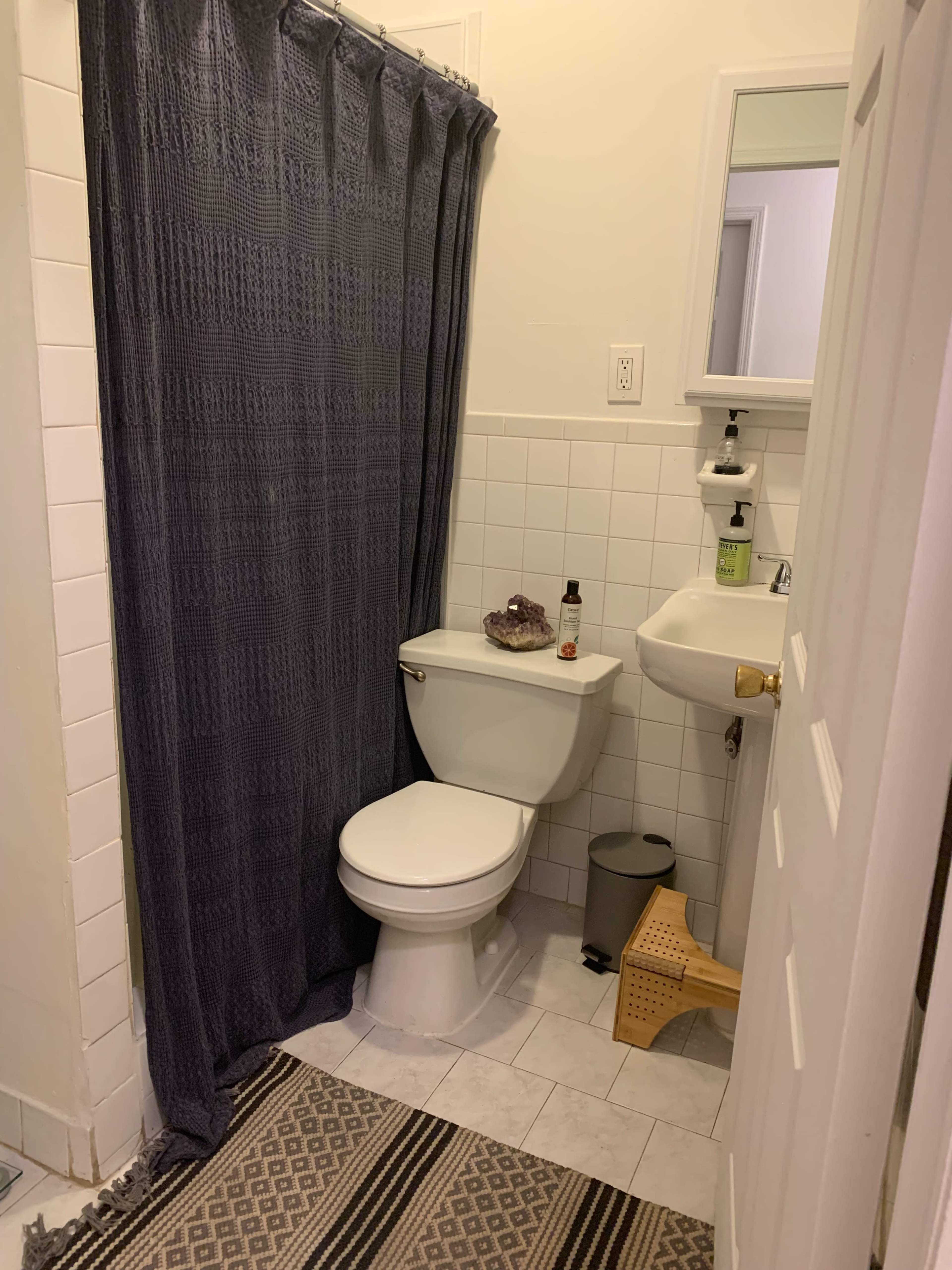 A small bathroom featuring a toilet, a sink, a shower curtain, and tiled flooring.