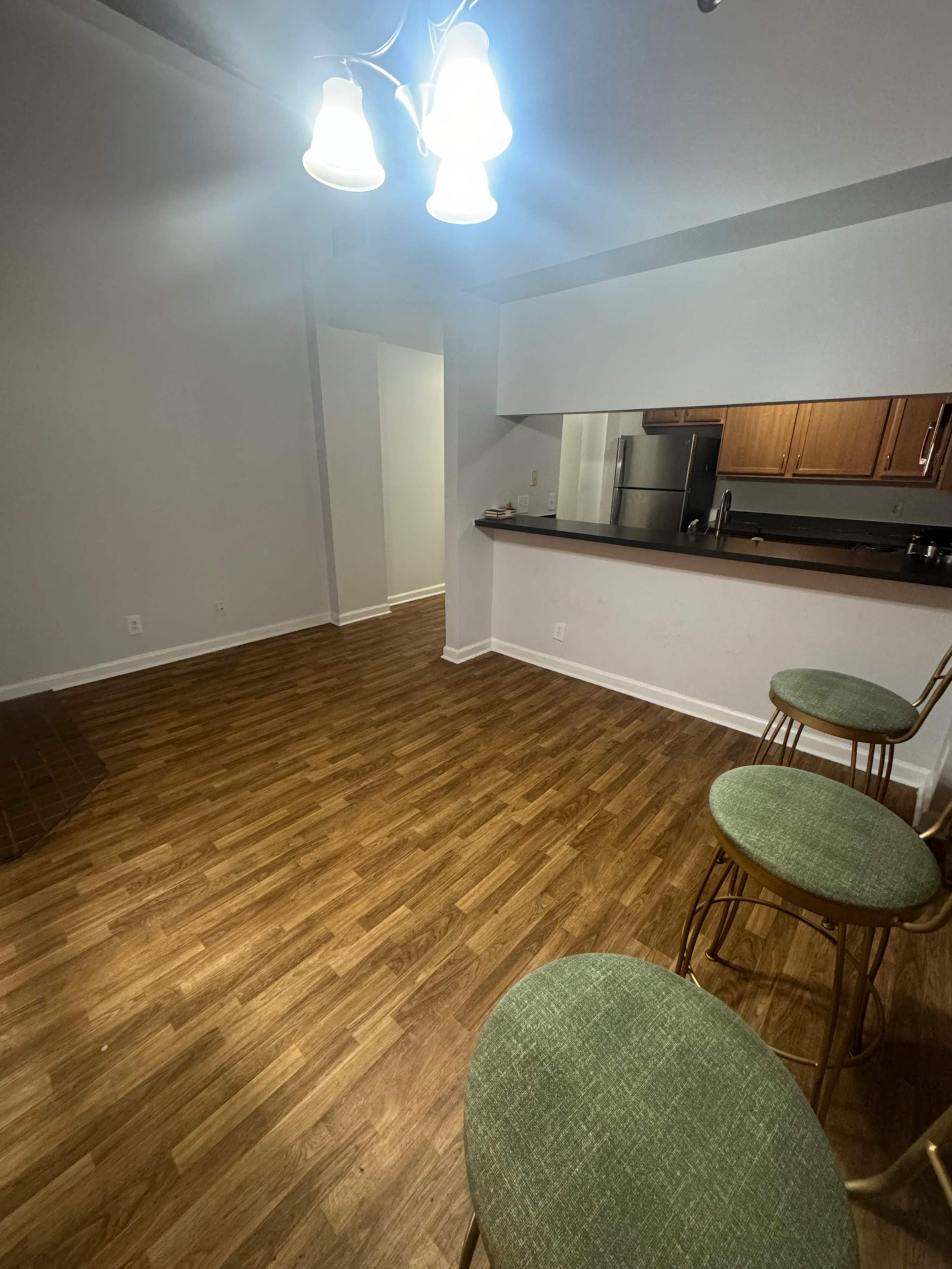A well-lit room features a bar area with three green-stooled chairs and a kitchen visible in the background.