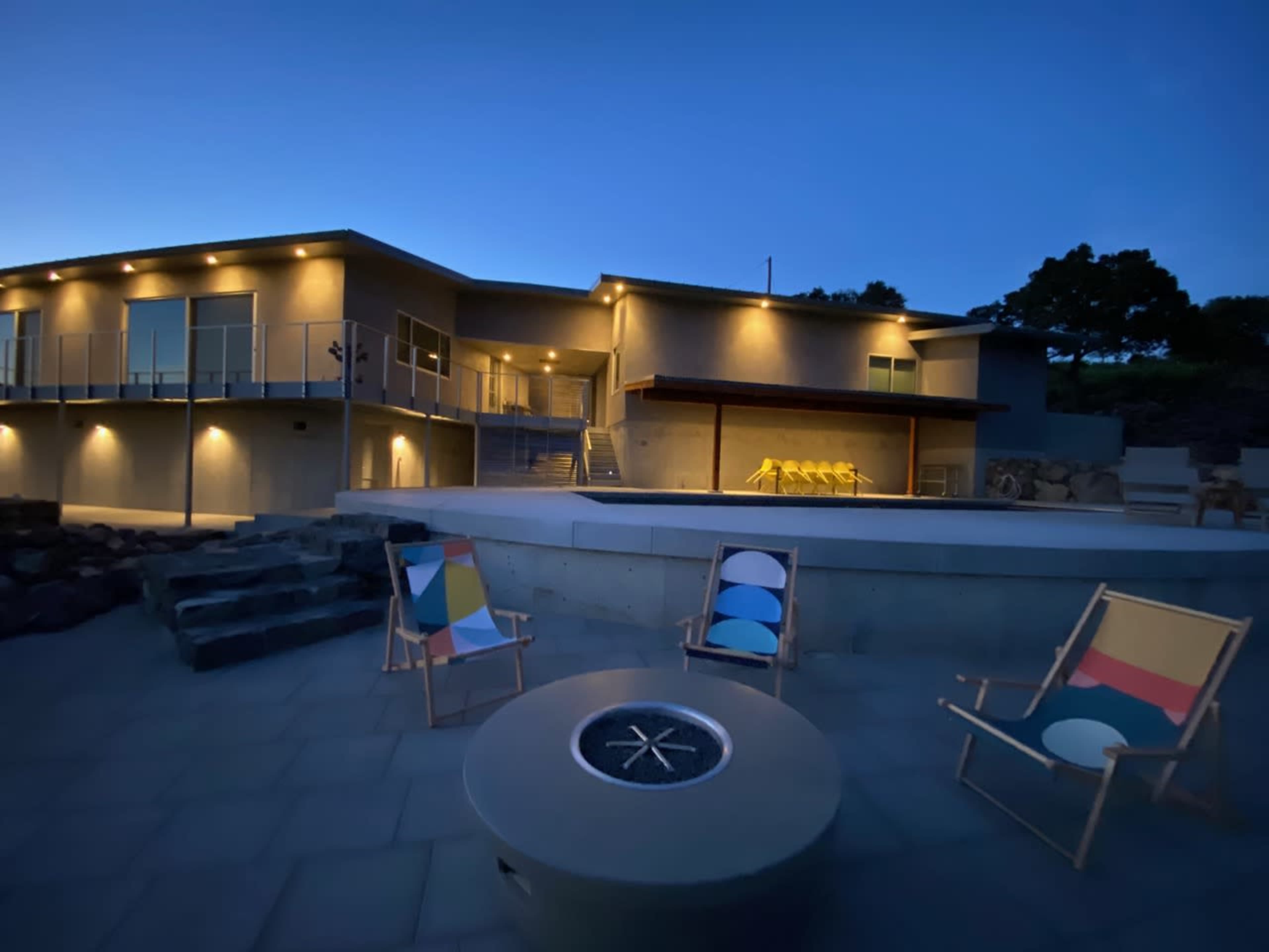 A modern house with outdoor seating and a pool is illuminated at dusk.