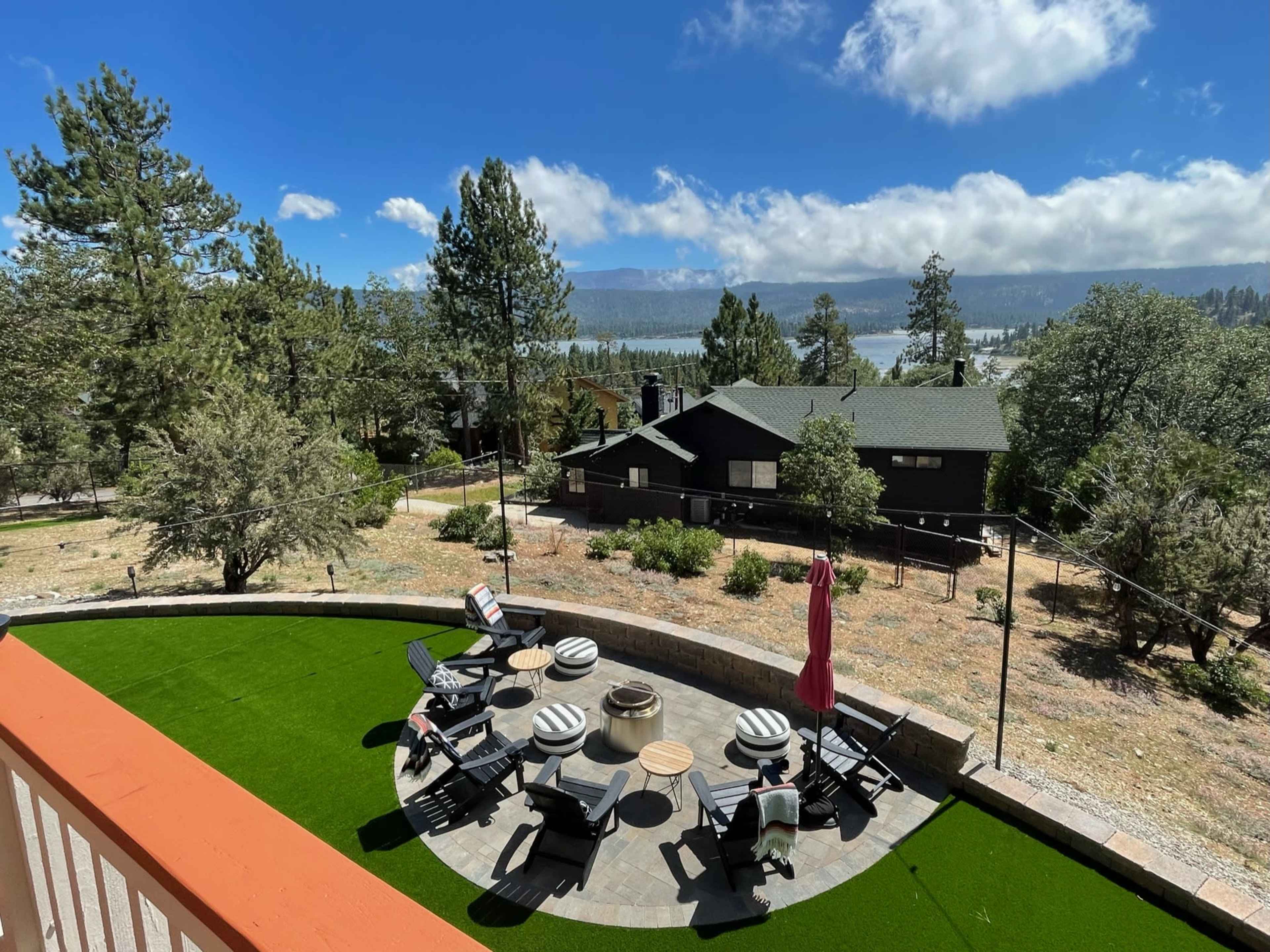 A landscaped outdoor area with seating arrangements around a fire pit, surrounded by trees and mountains in the background.