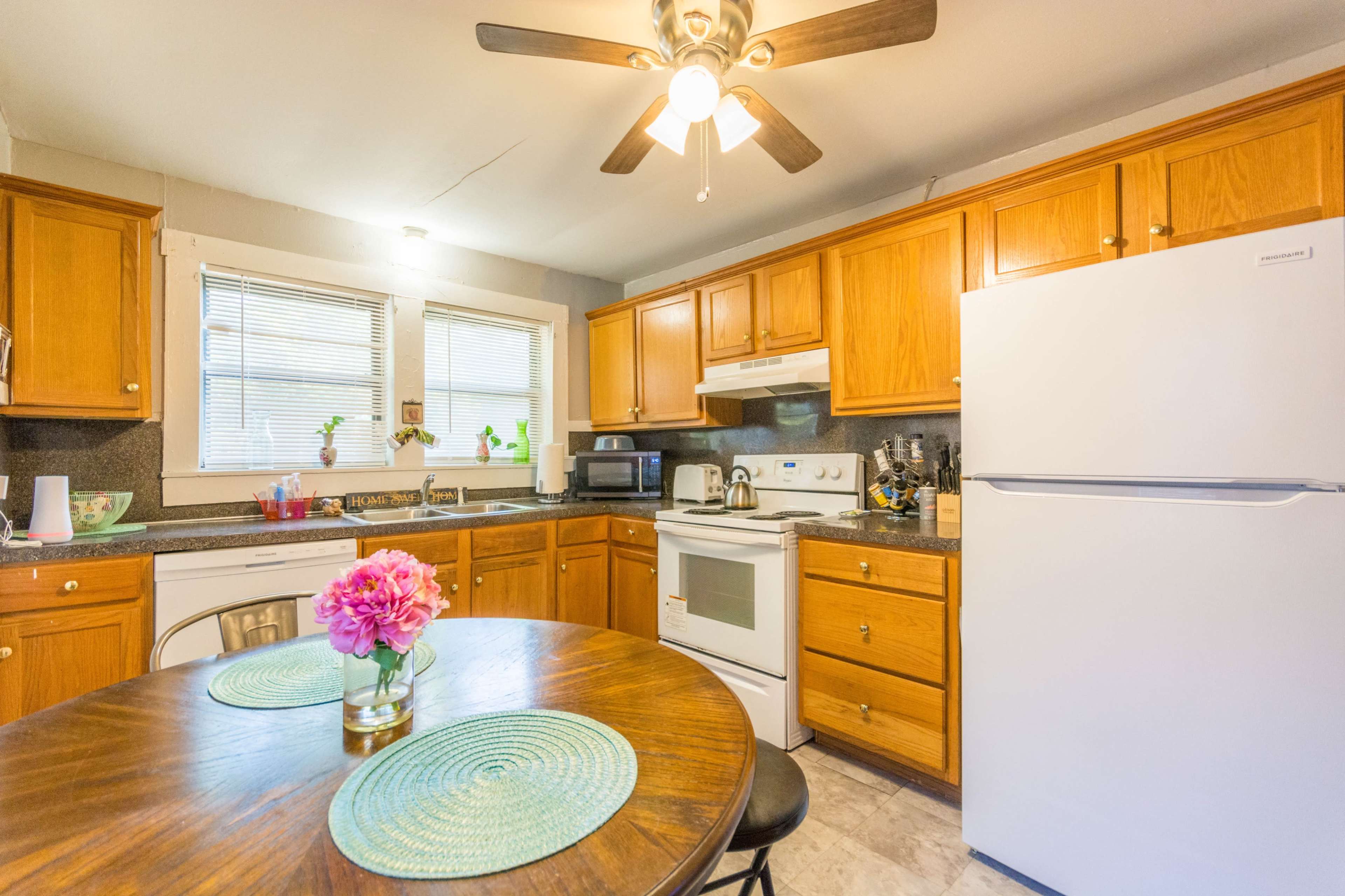 A kitchen features wooden cabinets, a white refrigerator, a round table with floral decorations, and appliances including a microwave and oven.