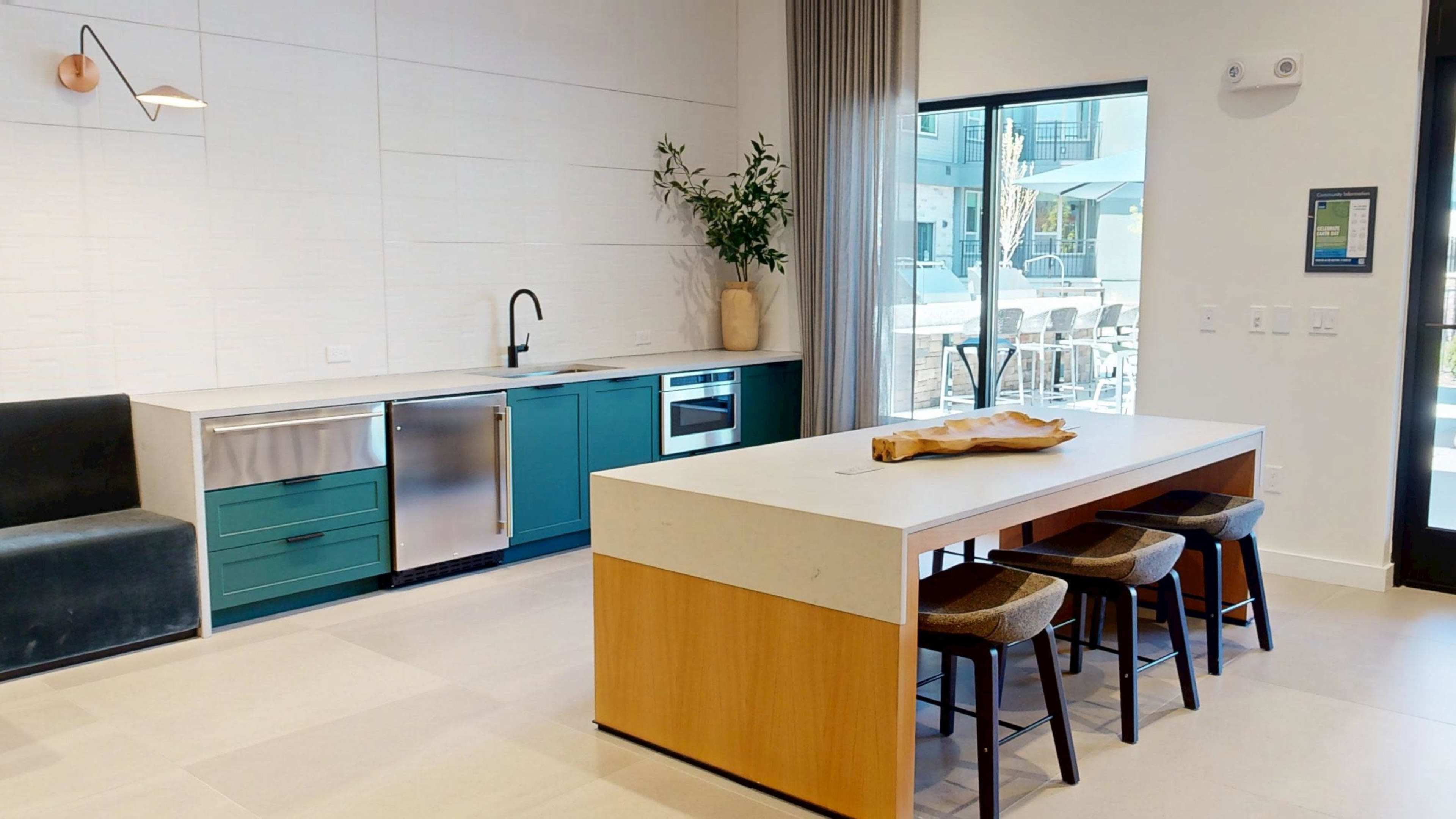 The image shows a modern kitchen with a large island, featuring a sink, a stovetop, and sleek cabinetry in shades of teal and wood.