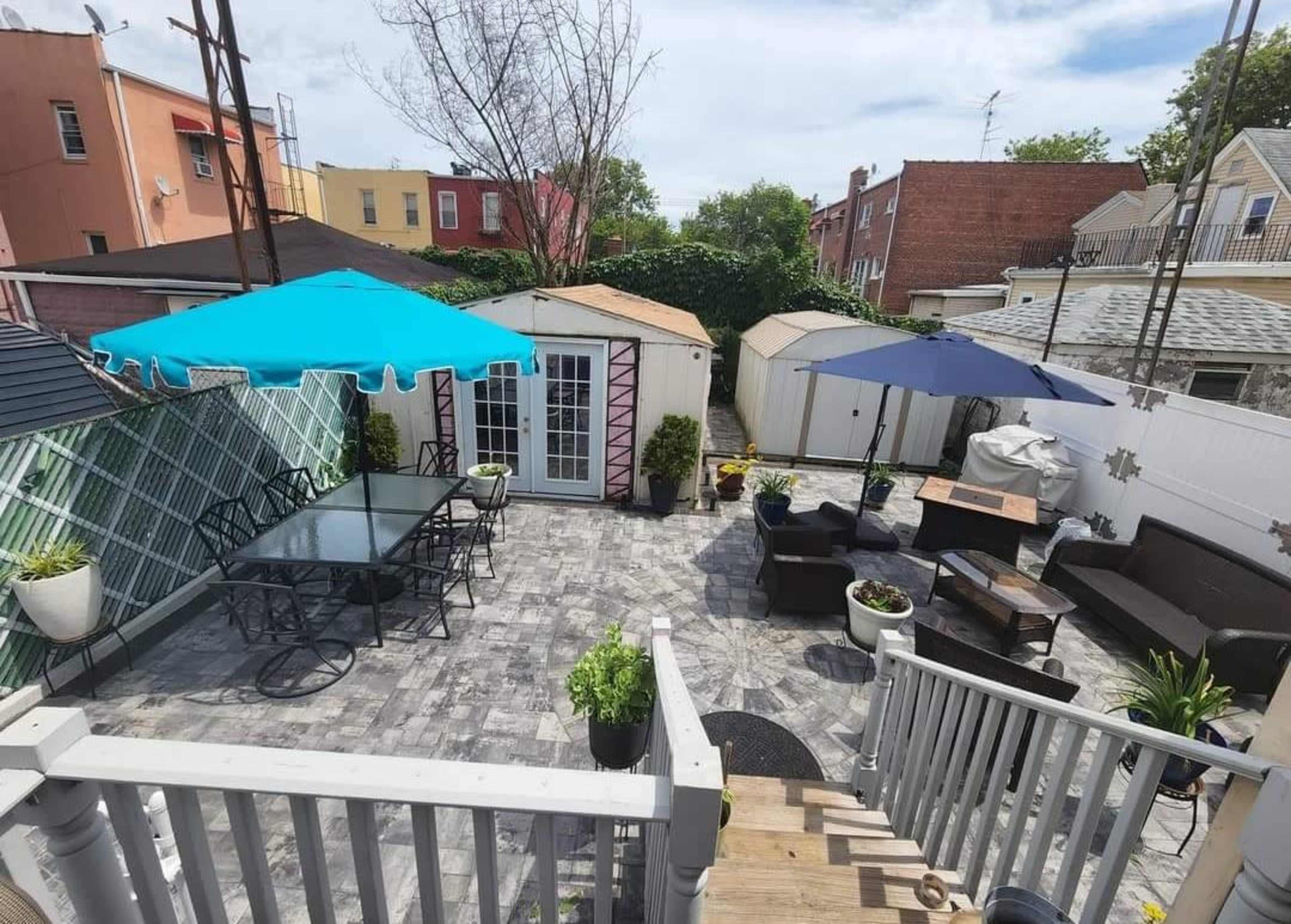 A well-arranged outdoor patio area with two shaded seating sections, a small shed, and various potted plants.