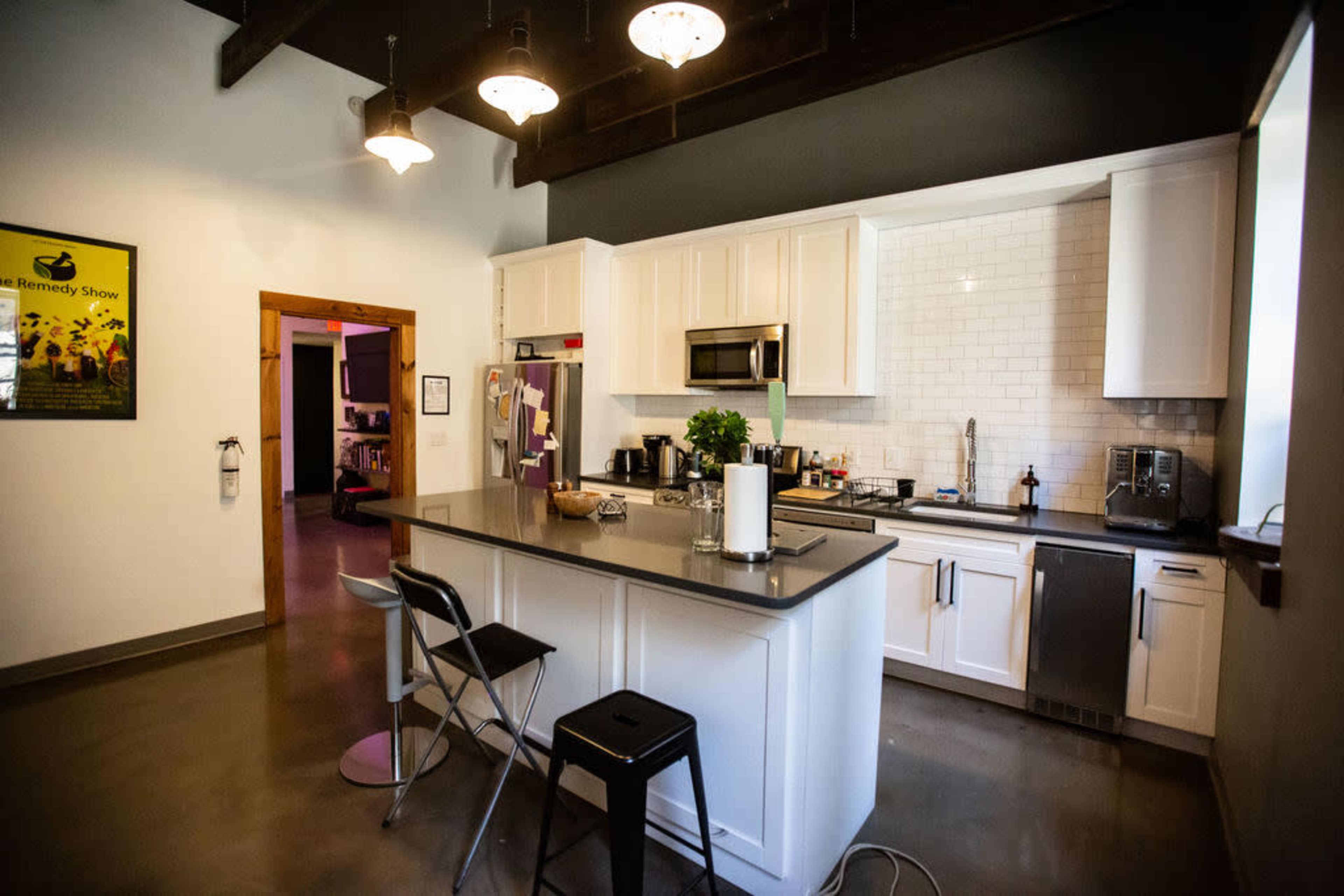 The image shows a modern kitchen with a central island, white cabinetry, stainless steel appliances, and stylish fixtures.