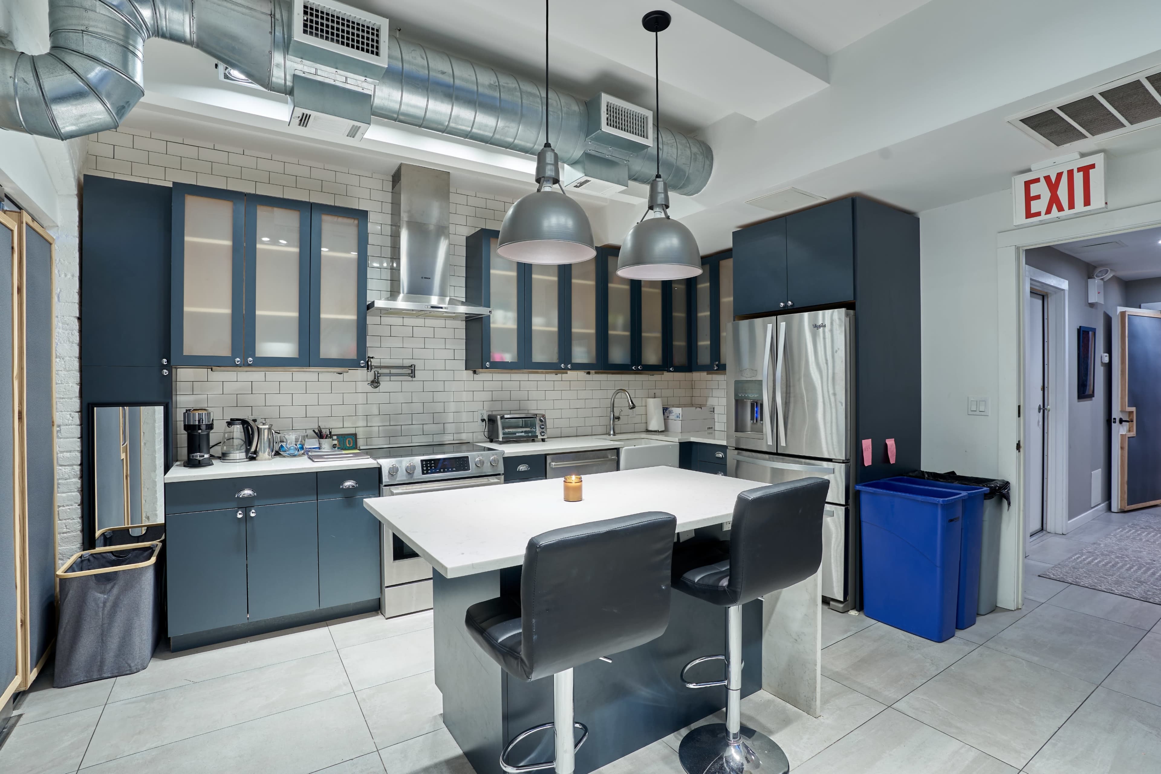 The kitchen features a central island with two black bar stools, dark cabinetry, stainless steel appliances, and exposed ductwork.