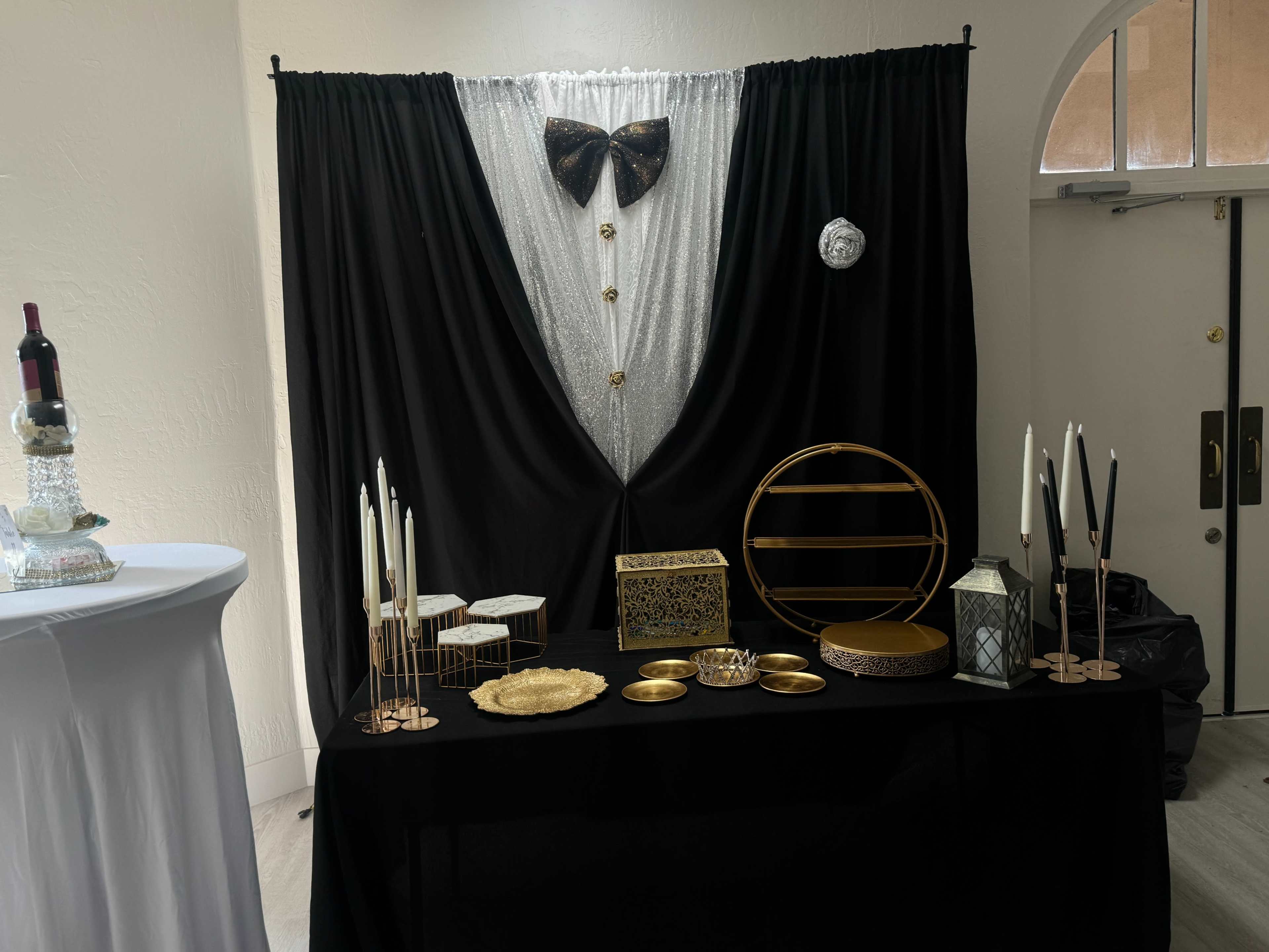 A decorative table features elegant gold and black accents, including a tuxedo-themed backdrop, candles, and assorted display items.