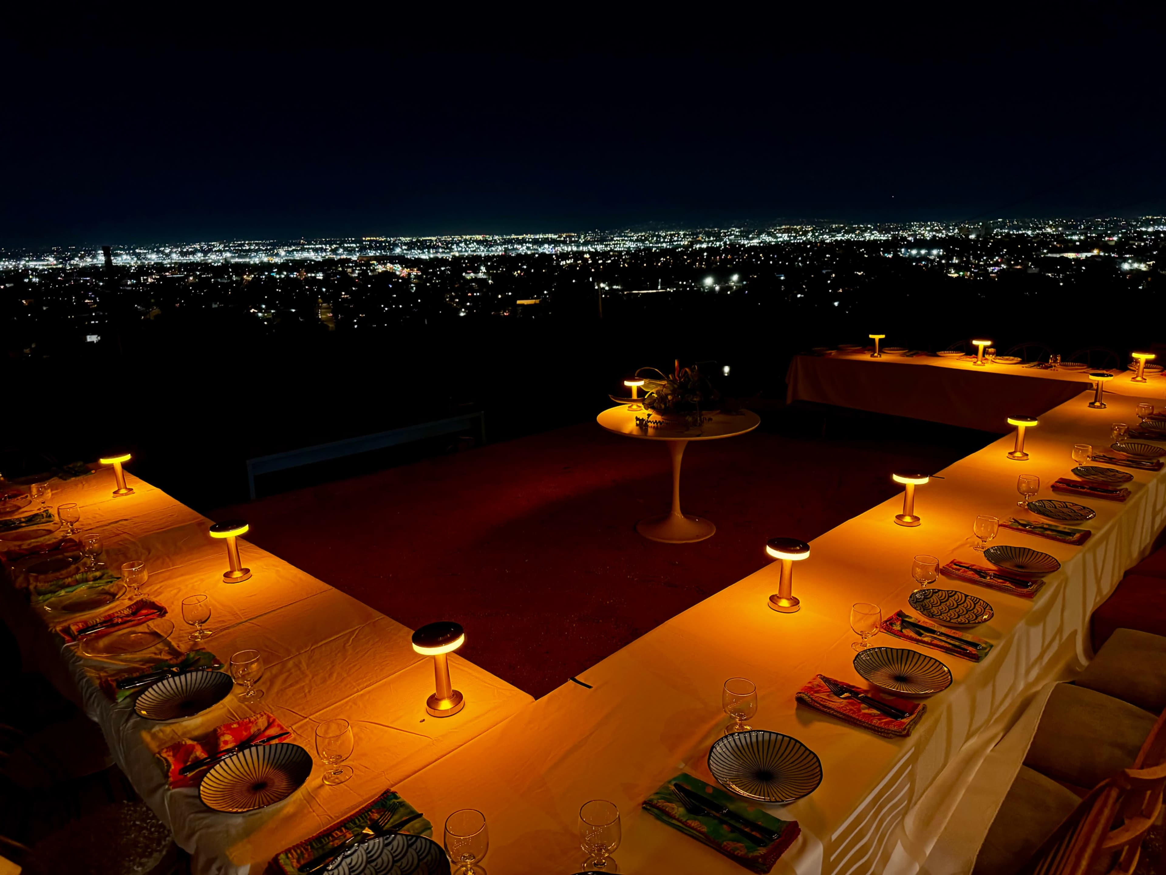 A table set for a dinner party is illuminated by glowing candles, overlooking a city sparkling with lights at night.