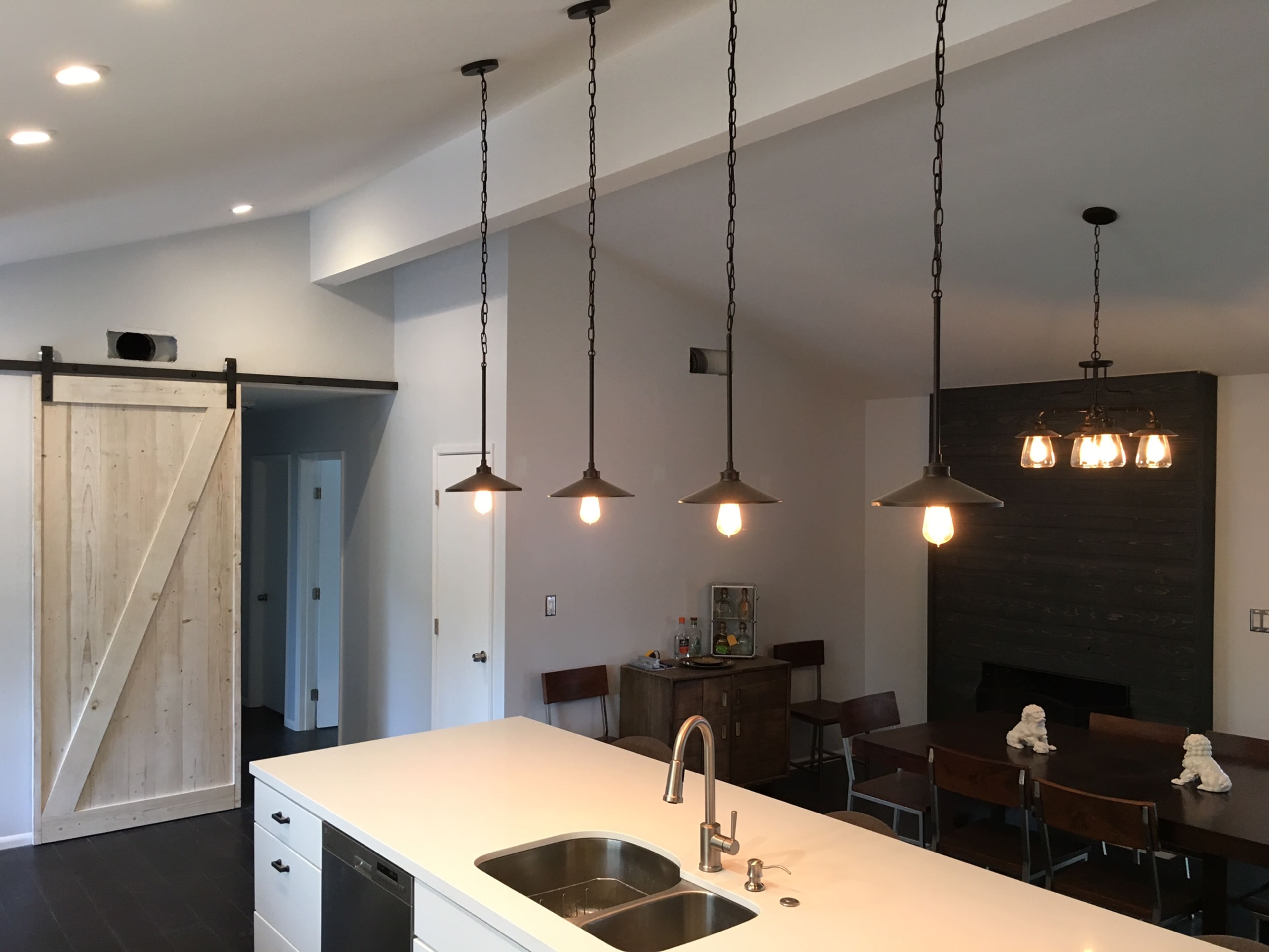 A modern kitchen features a large island with a double sink, pendant lighting, and a sliding barn door that leads to another room.
