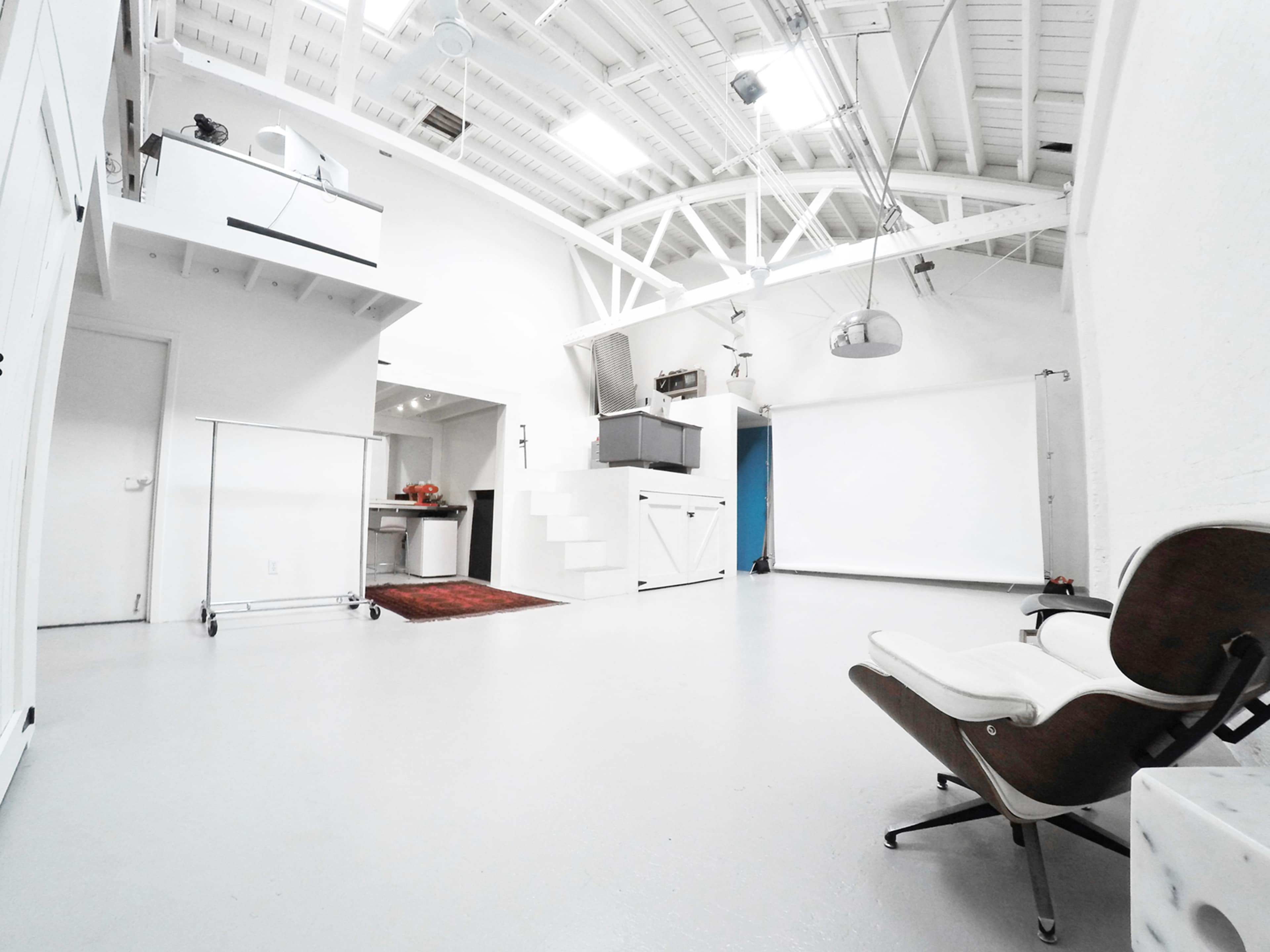 A spacious, minimalistic studio with white walls, a light gray floor, a staircase, and a large white backdrop for photography.
