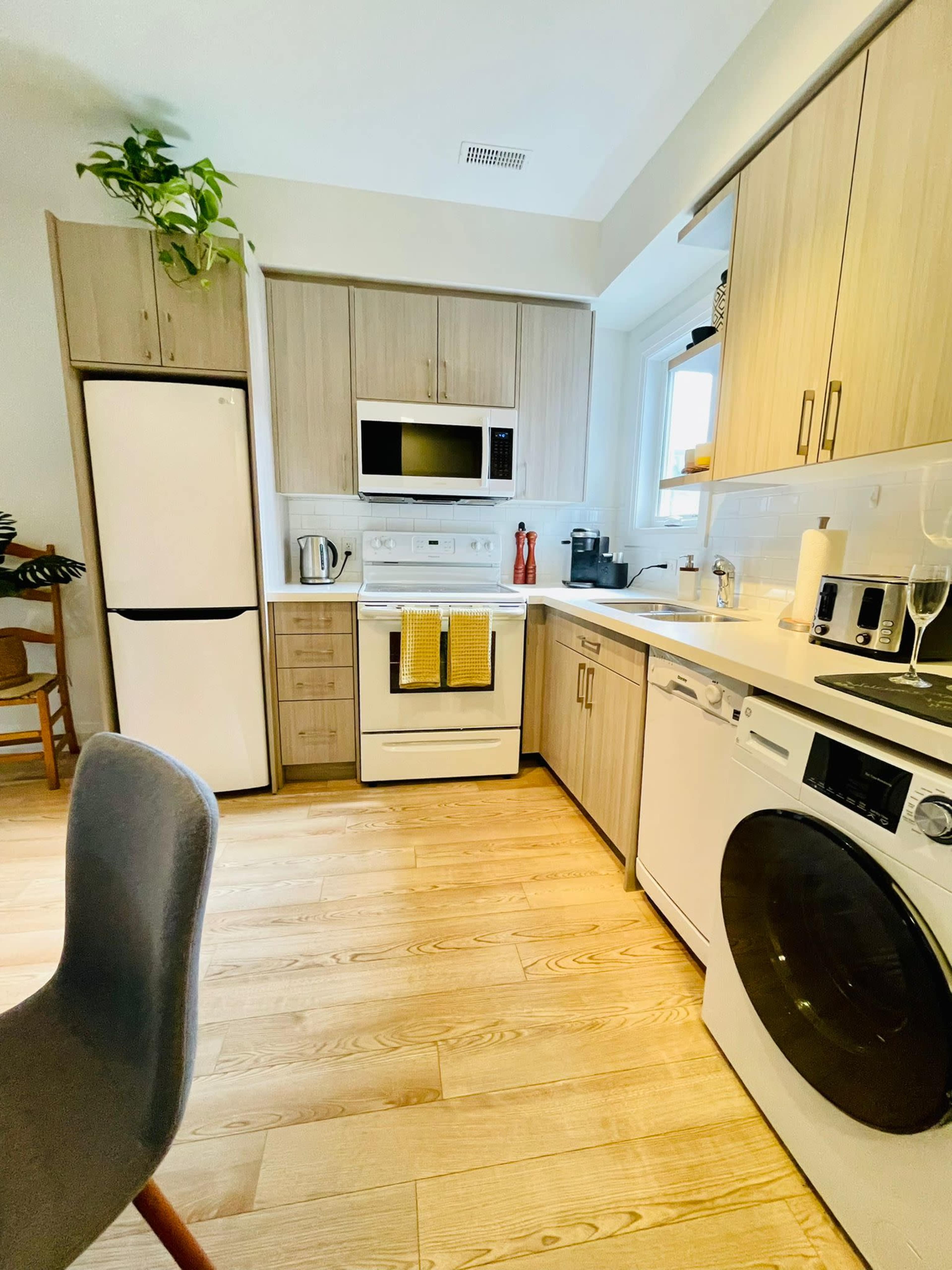 A modern kitchen with wooden cabinetry, a white refrigerator, an oven, and a washer-dryer combo, featuring light wood flooring.