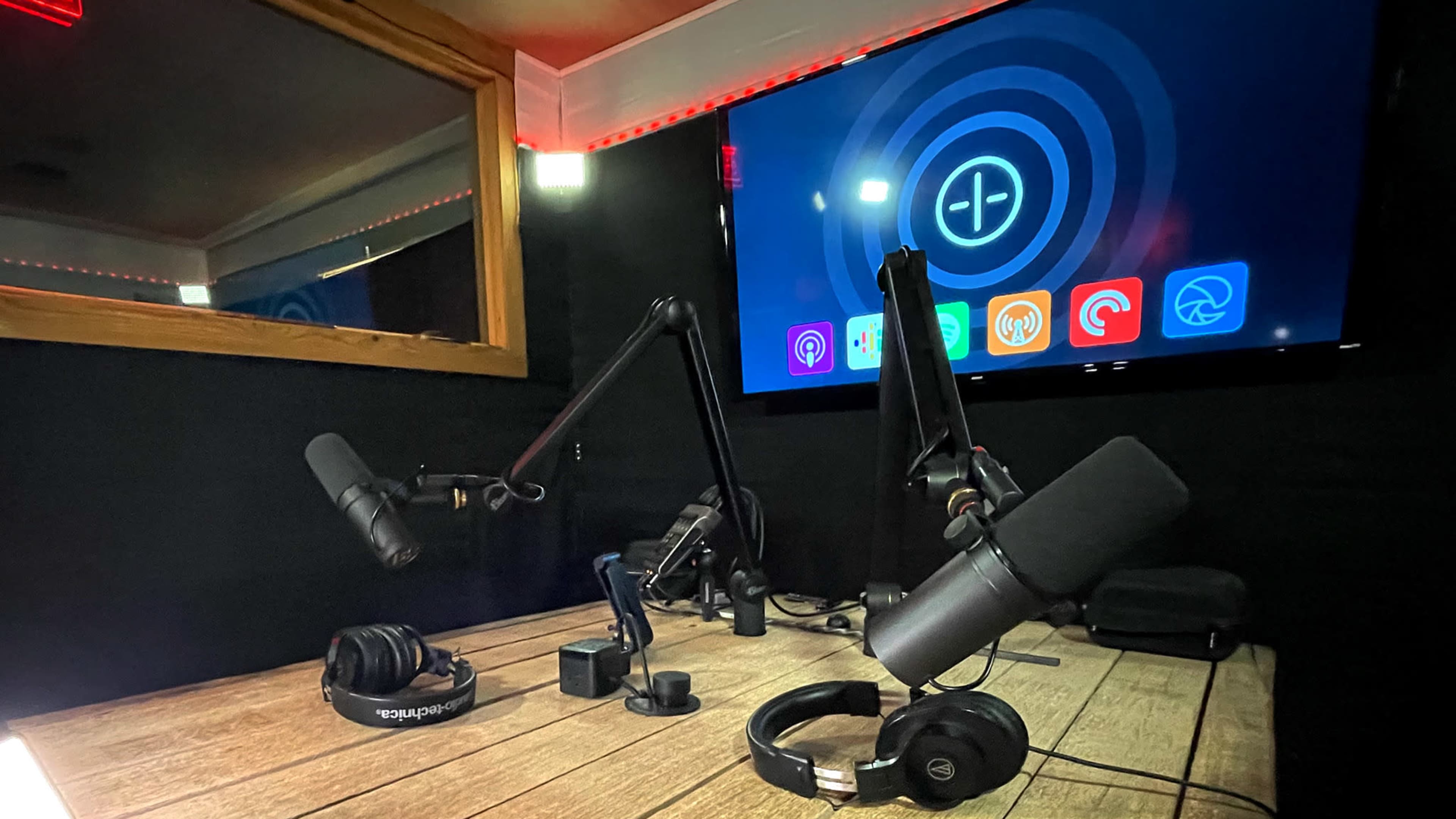 A podcast studio featuring multiple microphones, headphones, and a large screen displaying an app interface.