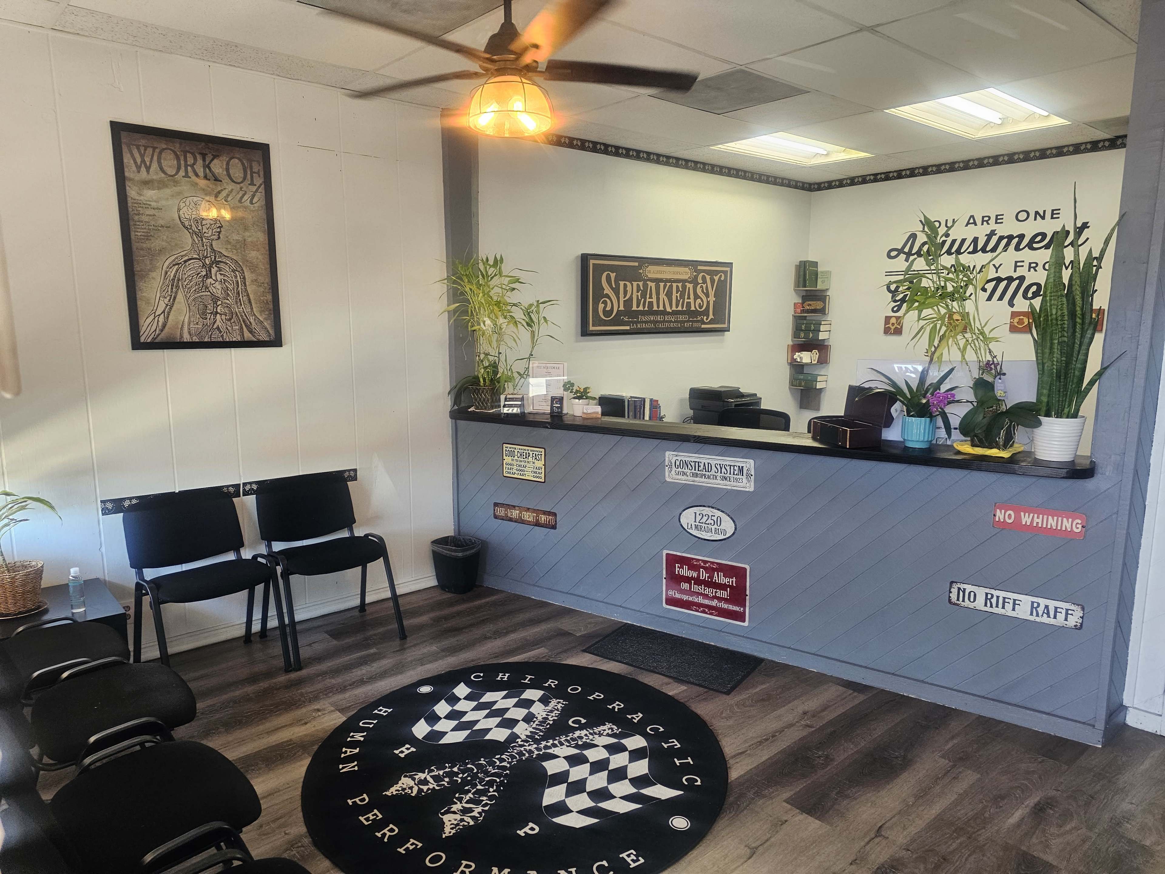The image shows a chiropractic clinic reception area with a front desk, seating for visitors, and various wall decorations.