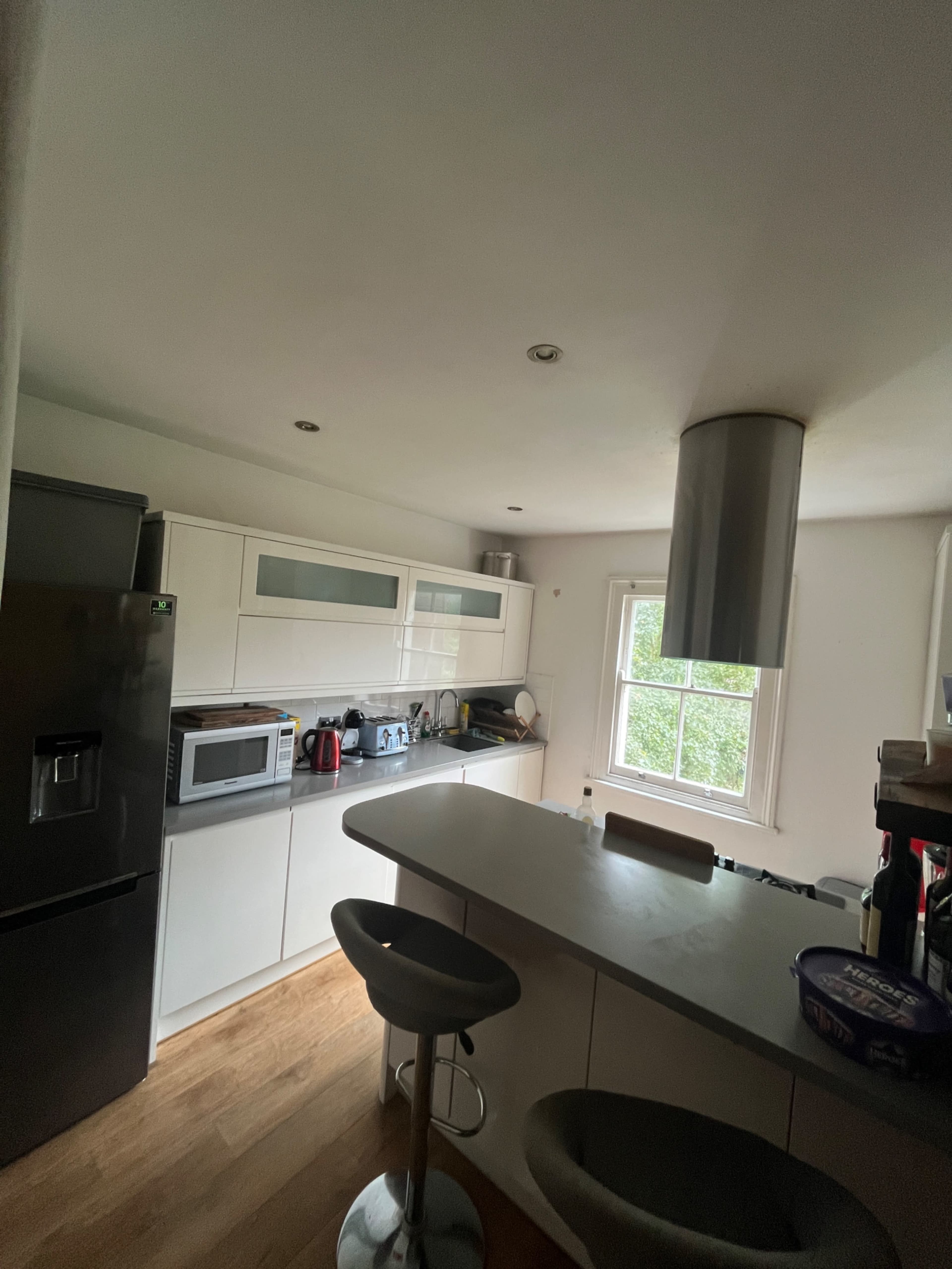 The image shows a modern kitchen with white cabinetry, a black refrigerator, a microwave, and a bar with stools.