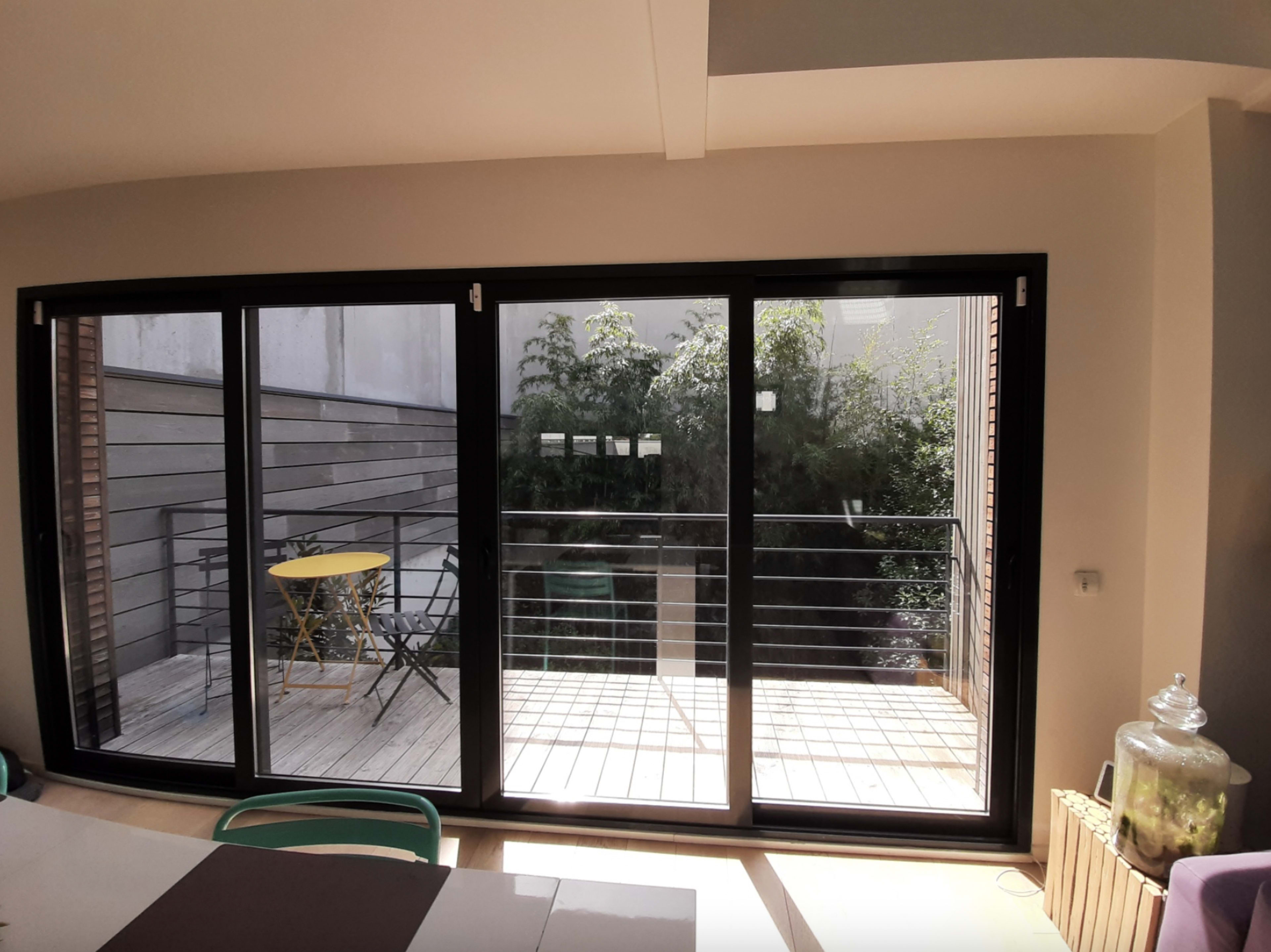 A modern indoor space with large glass doors opening to a wooden deck and greenery outside.