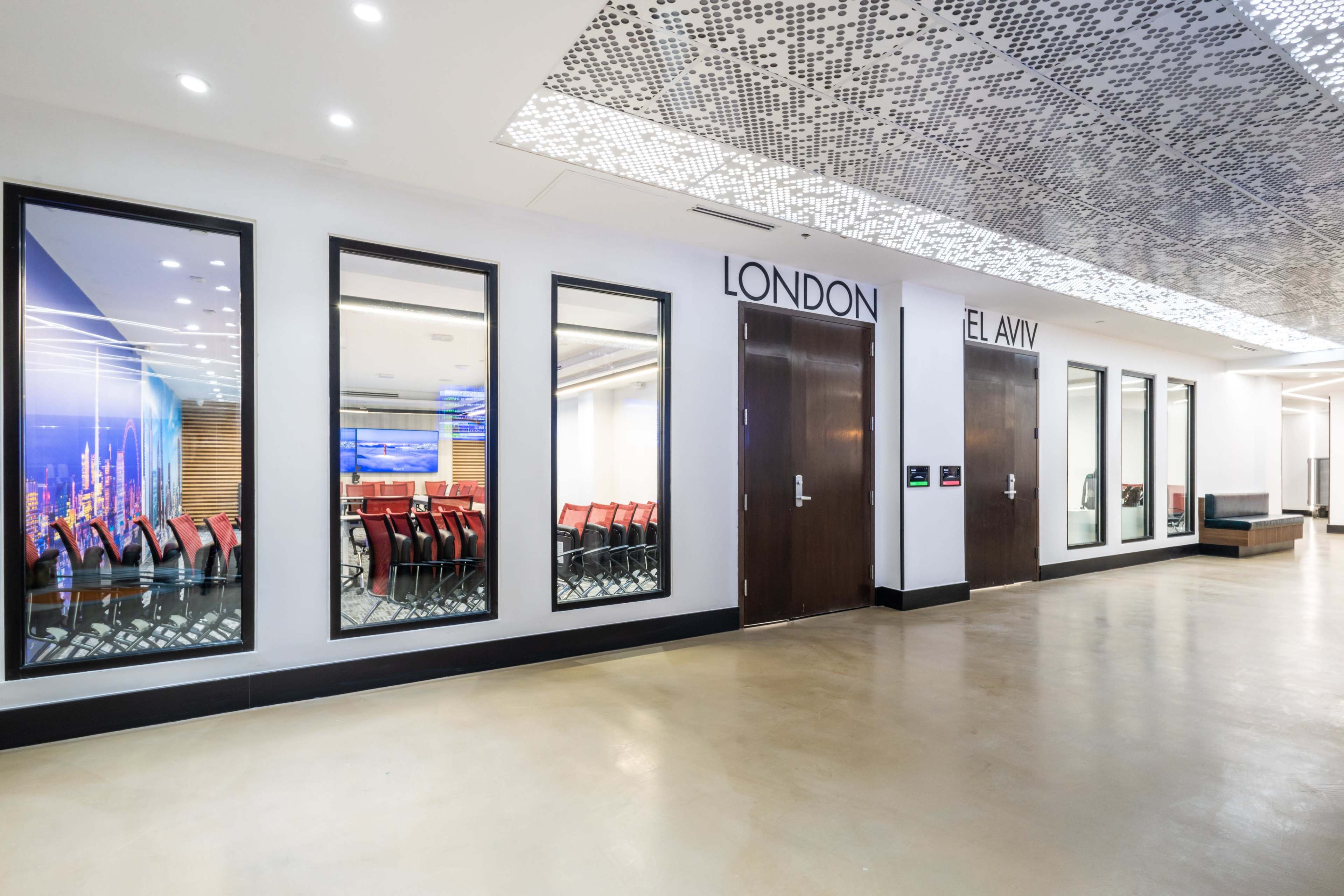 A modern hallway with two doors labeled "LONDON" and "TEL AVIV," featuring glass windows revealing empty rooms with chairs arranged for meetings.