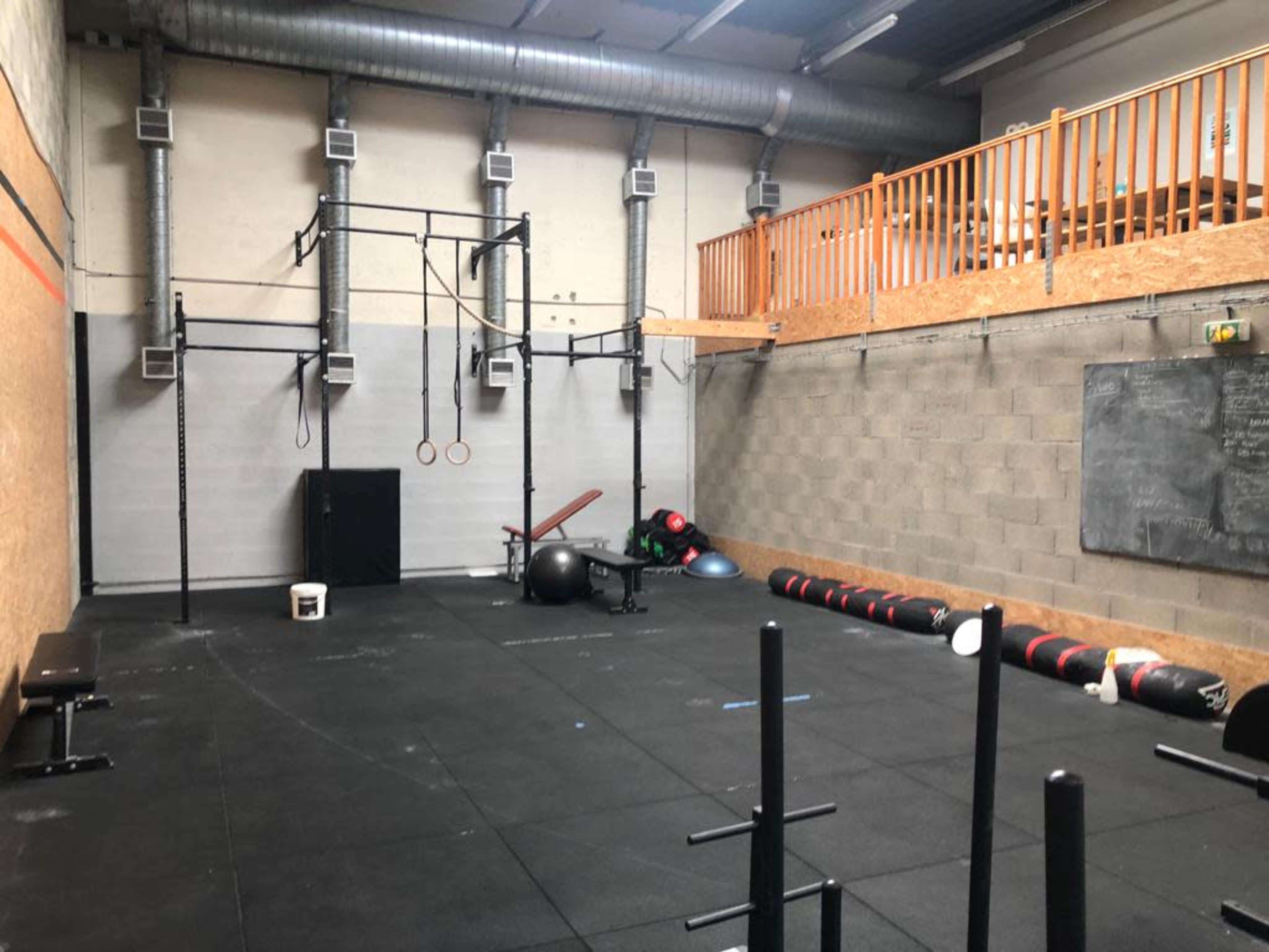 An empty gym with various exercise equipment, including a squat rack, rings, and a row of weighted balls, situated on a rubberized floor.