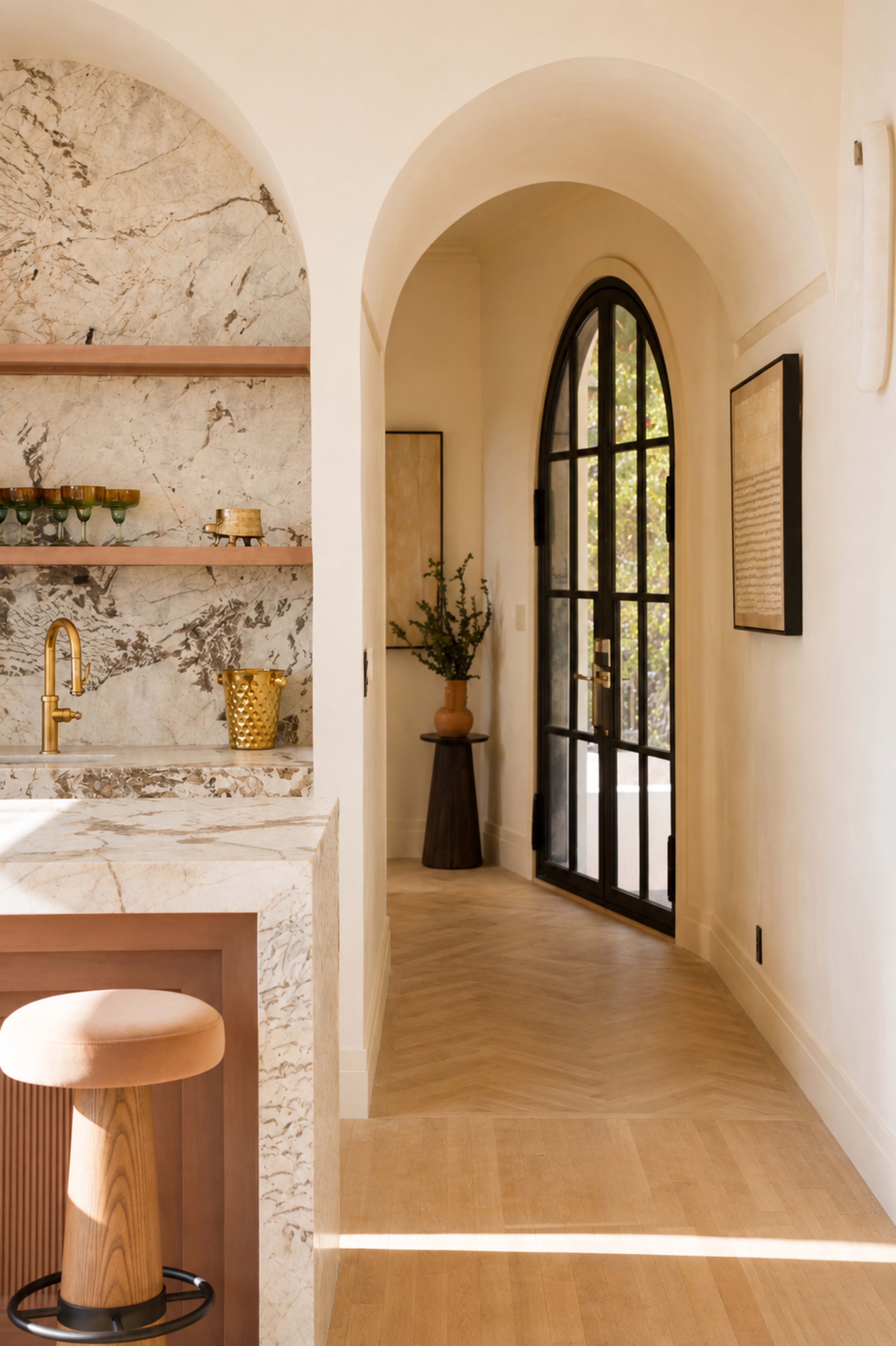 The image shows a softly lit interior featuring an arched doorway, a marble bar with a wooden stool, and elegant decor elements.
