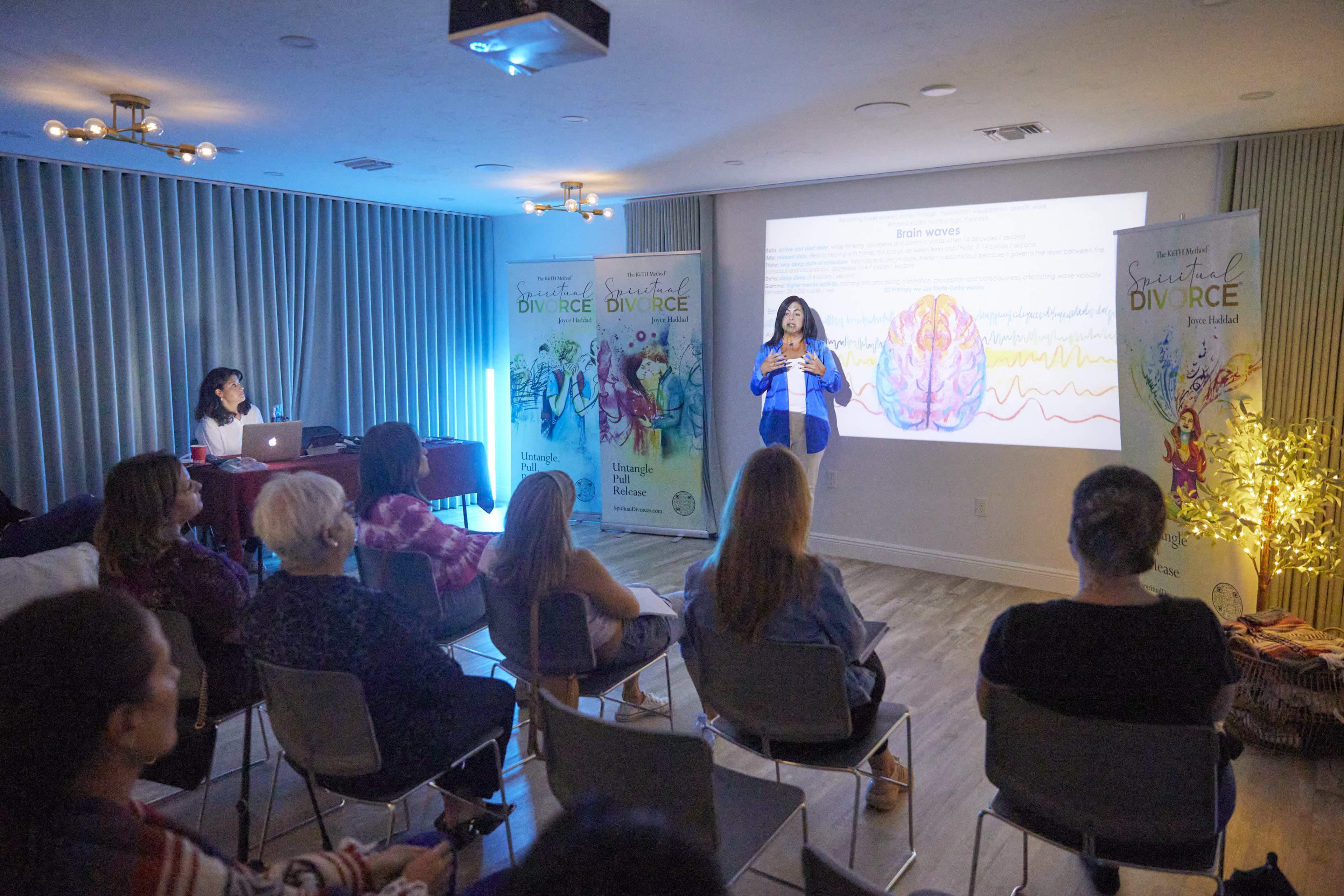 A speaker presents information on brain waves to an audience seated in a modern conference room with banners in the background.