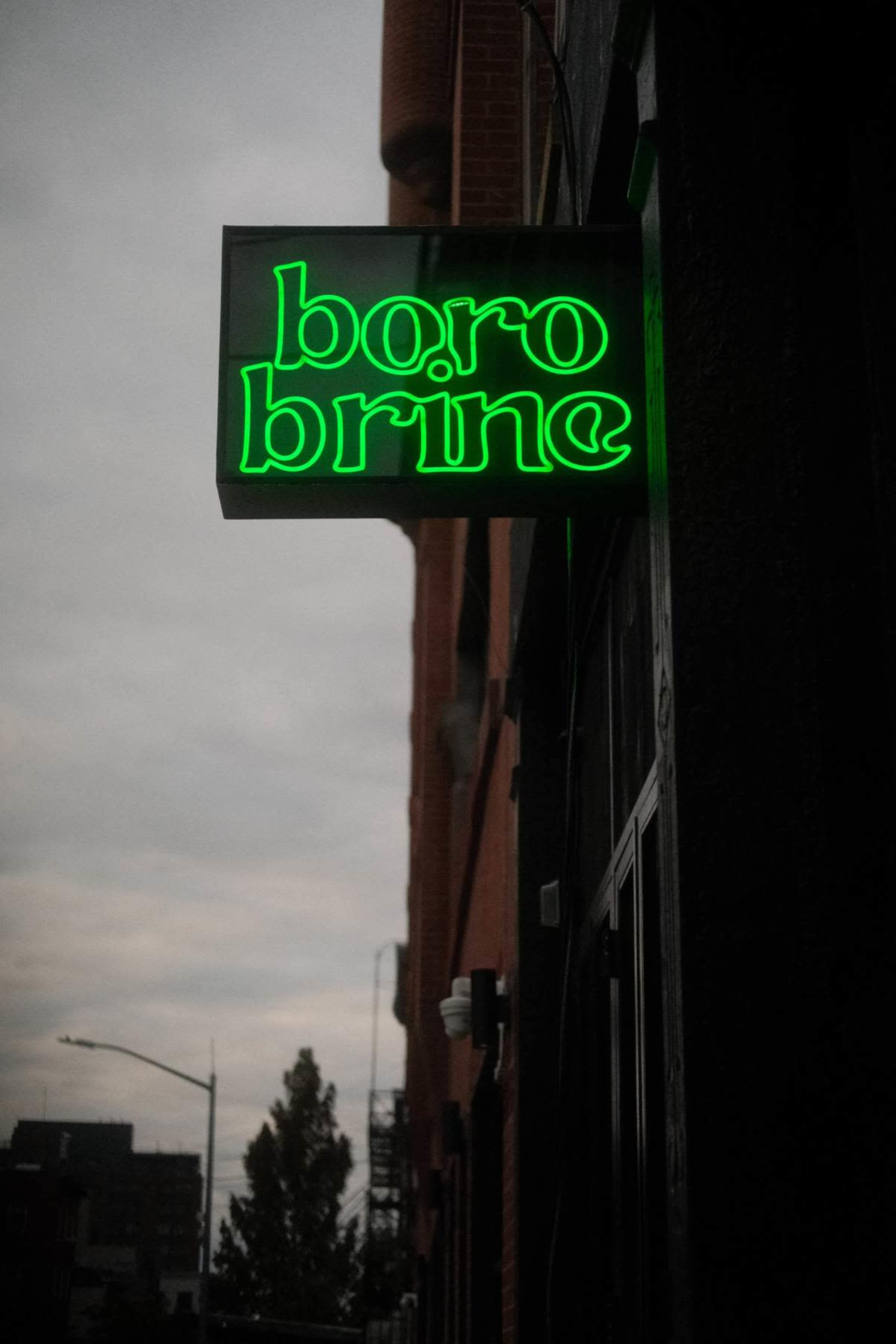 A neon sign reading "boro brine" hangs outside a building on a cloudy day.