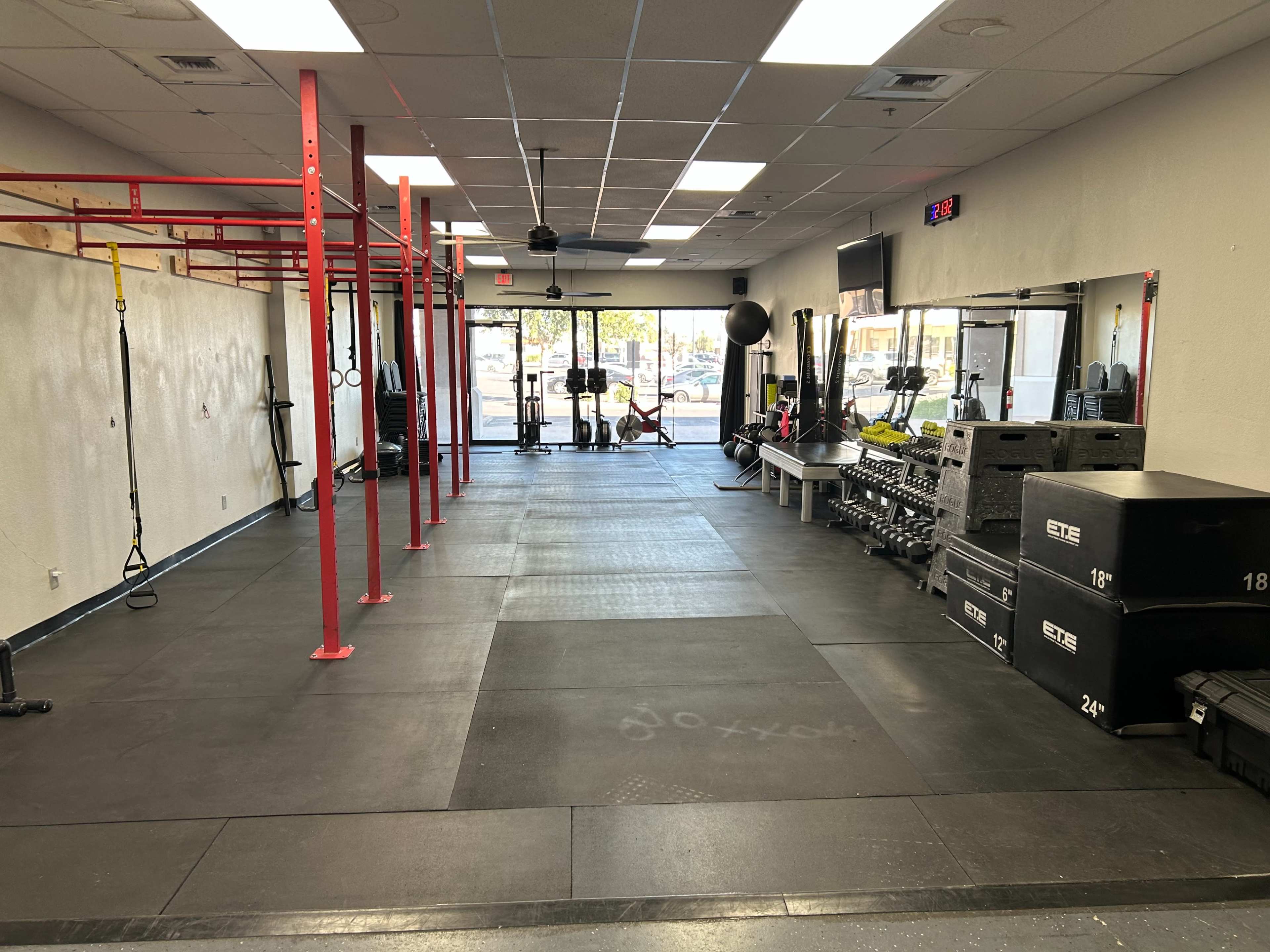 The image shows an interior of a gym with workout equipment, including red pull-up bars, weight racks, and a large mirror along one wall.