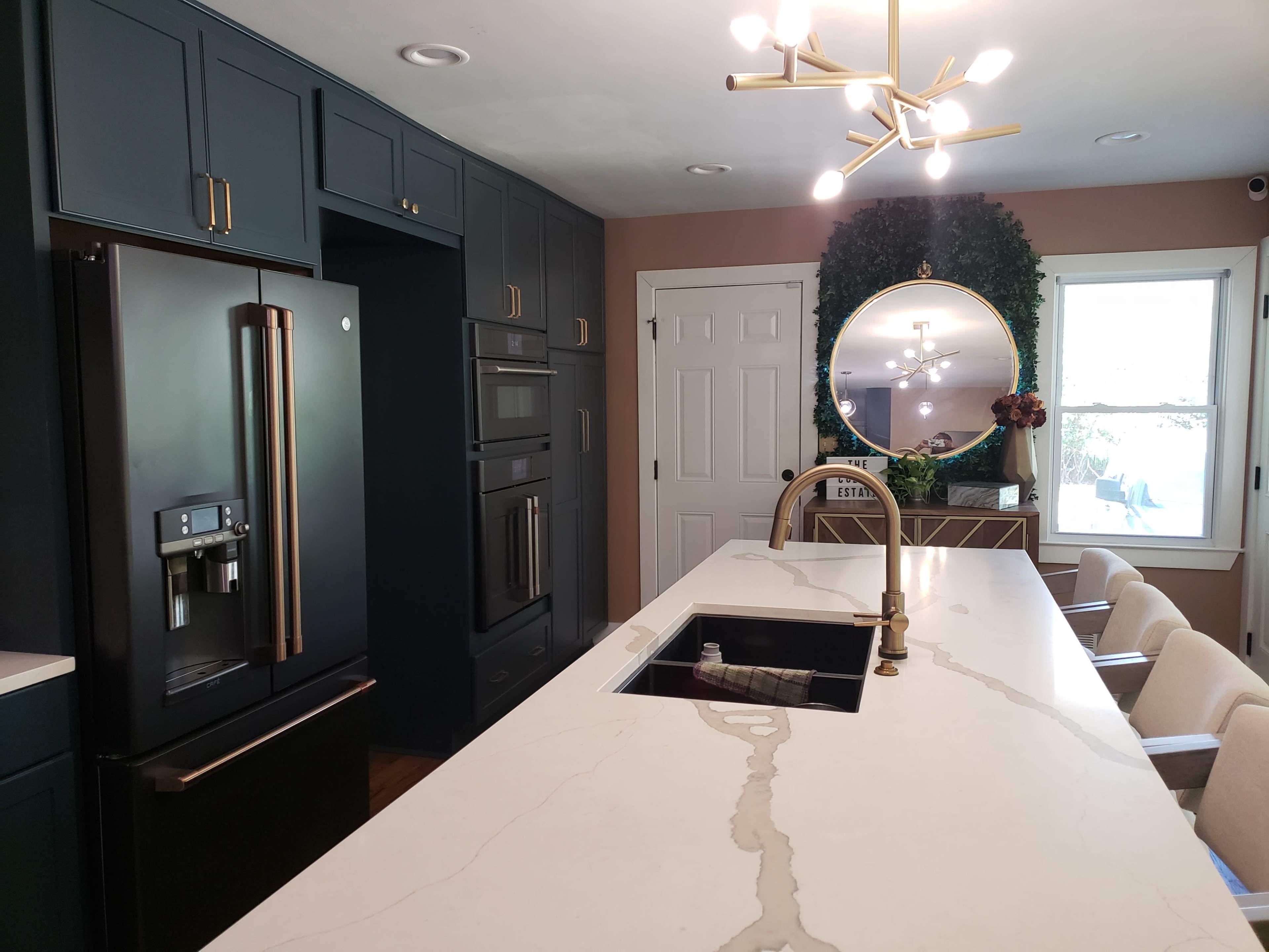 The kitchen features dark cabinetry, a large island with a marble countertop, and modern appliances, including a black refrigerator and wall oven.