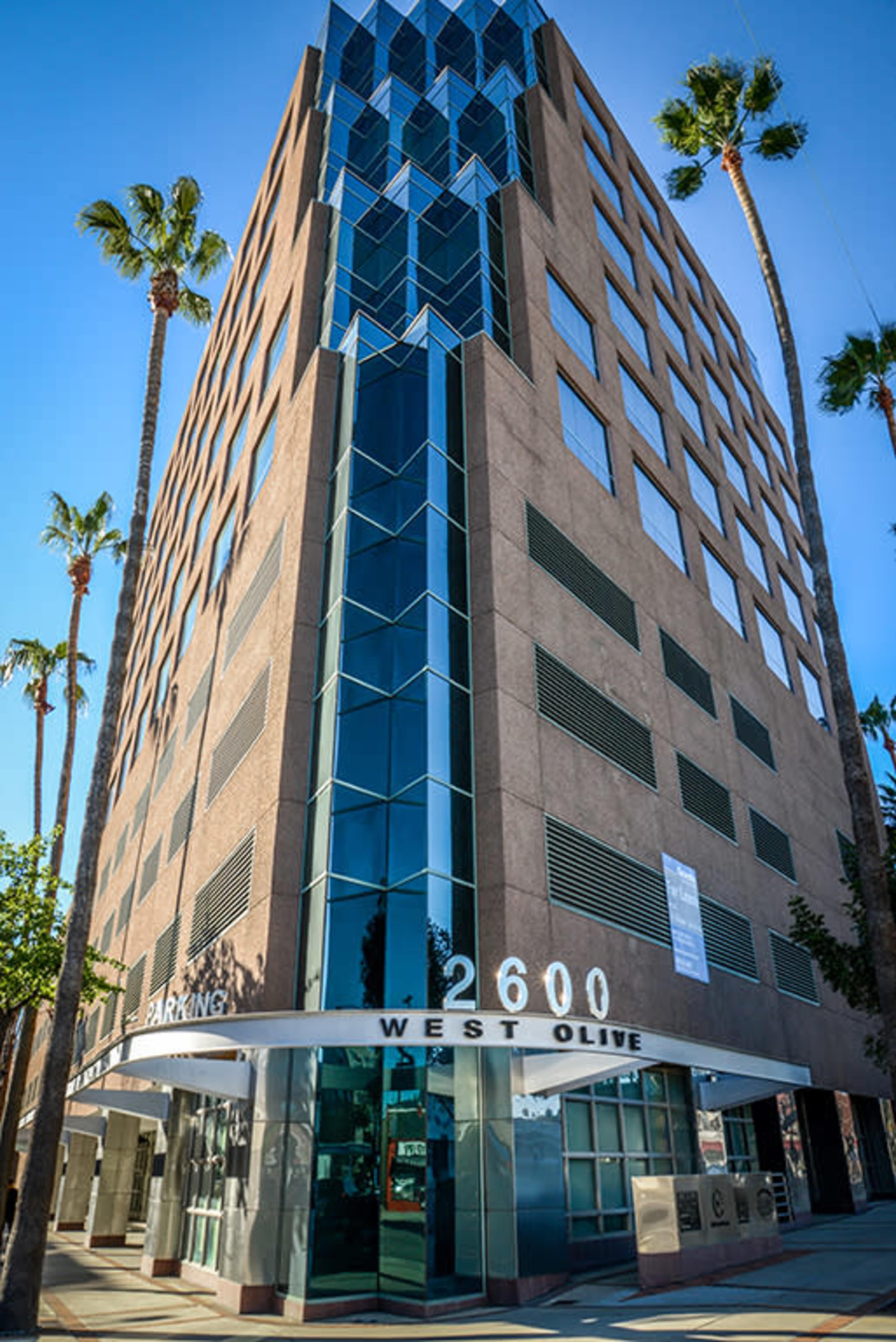 A multi-story office building at 2600 West Olive, featuring large glass windows and palm trees aligned along the sidewalk.