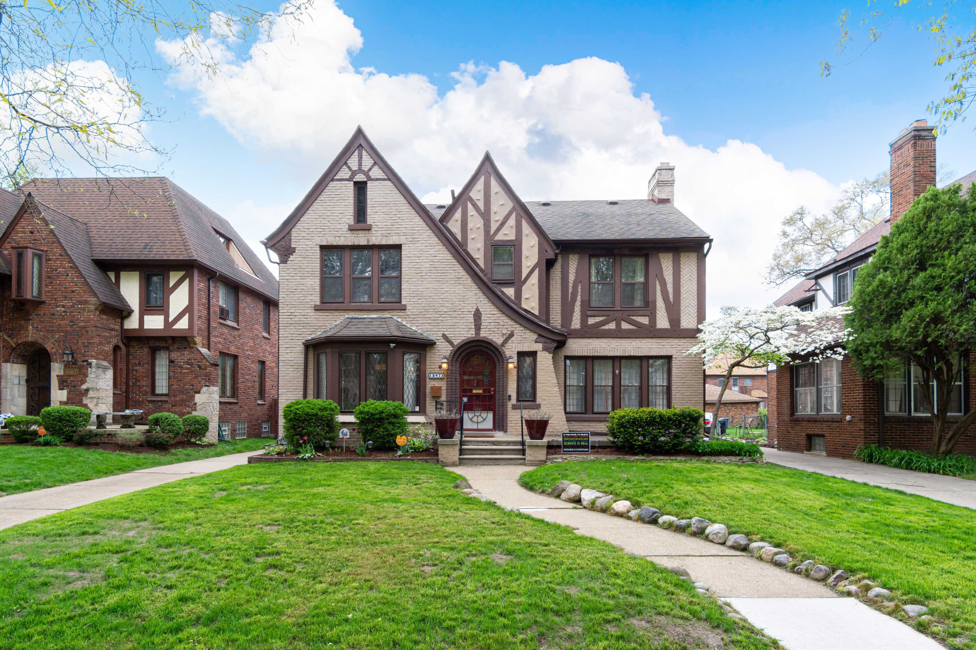 A two-story Tudor-style house with a brick and stucco façade is surrounded by manicured lawns and landscaped gardens.