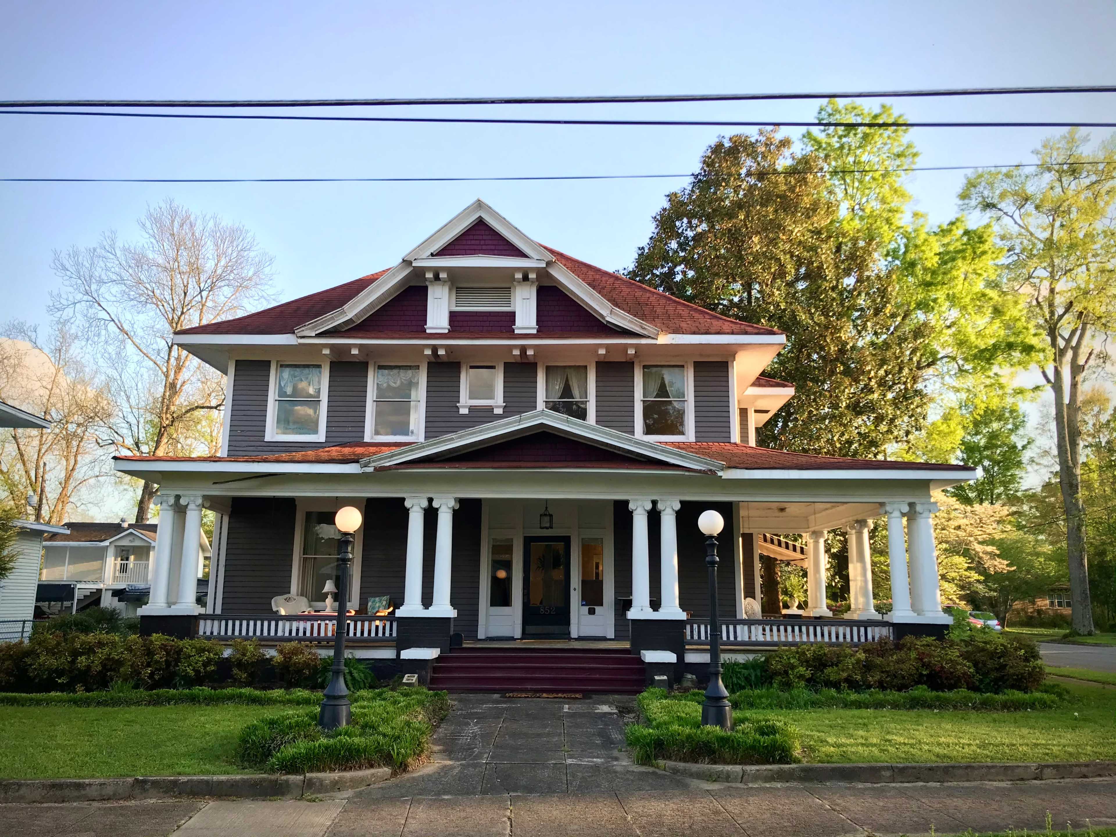 A large, two-story Victorian-style house features a red roof, white columns, and a wide front porch.