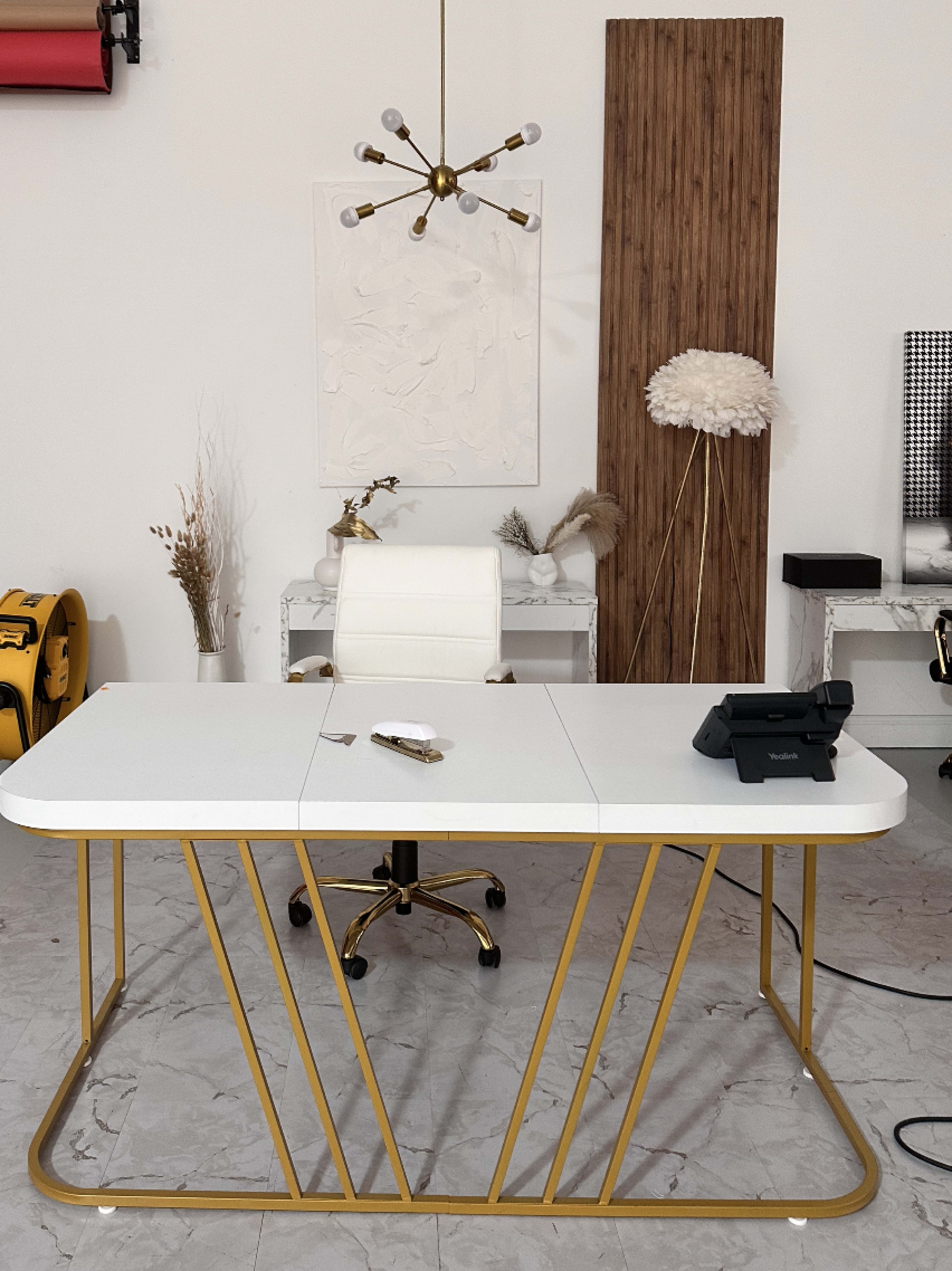 A modern office setup features a white desk with a gold base, a white chair, a telephone, and decorative items in a minimalist space.