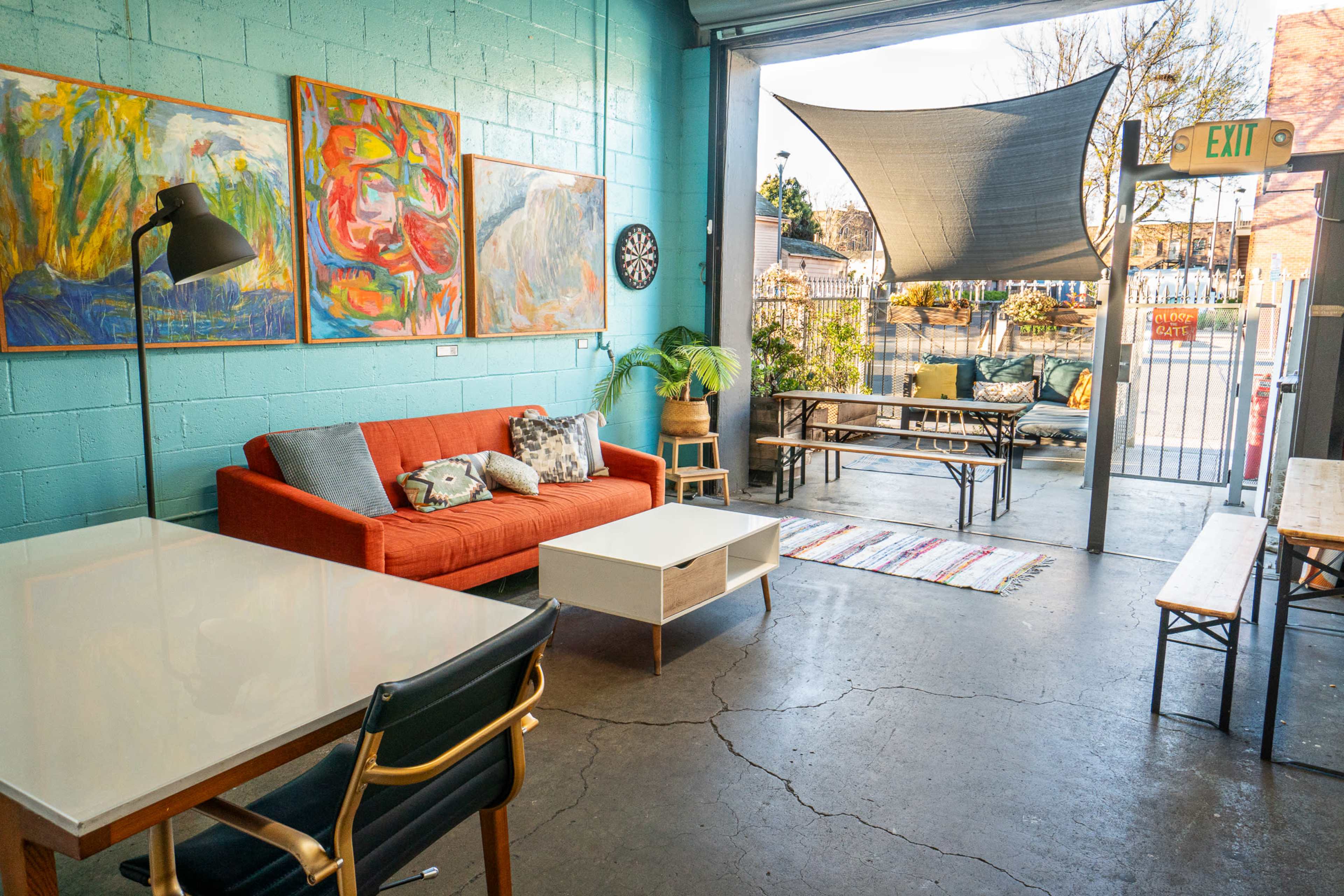 The image shows a bright, modern lounge area with a red couch, a white coffee table, and a large window that opens to an outdoor seating space.
