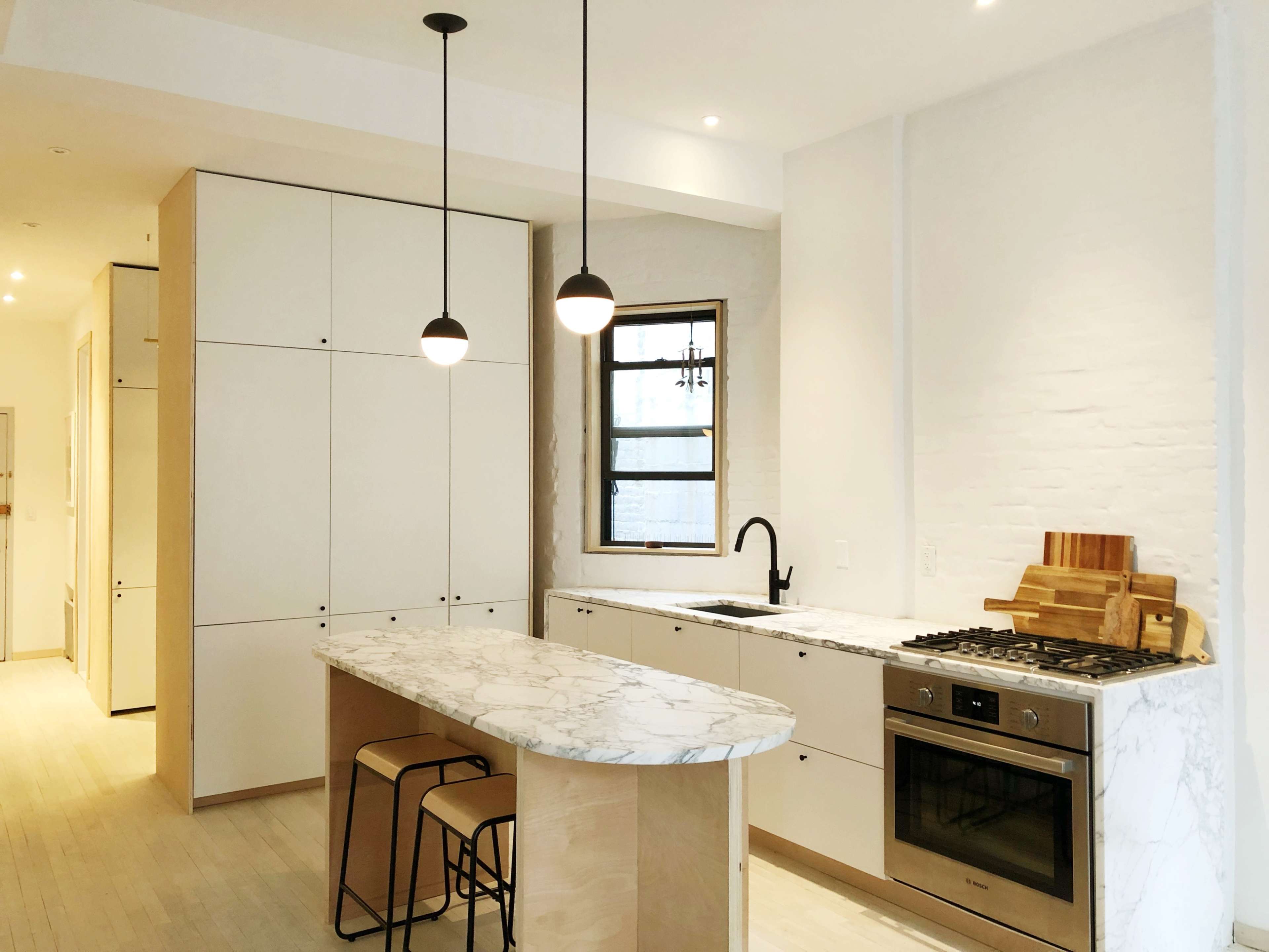 A modern kitchen features a marble-topped island, sleek cabinetry, stainless steel appliances, and pendant lighting.