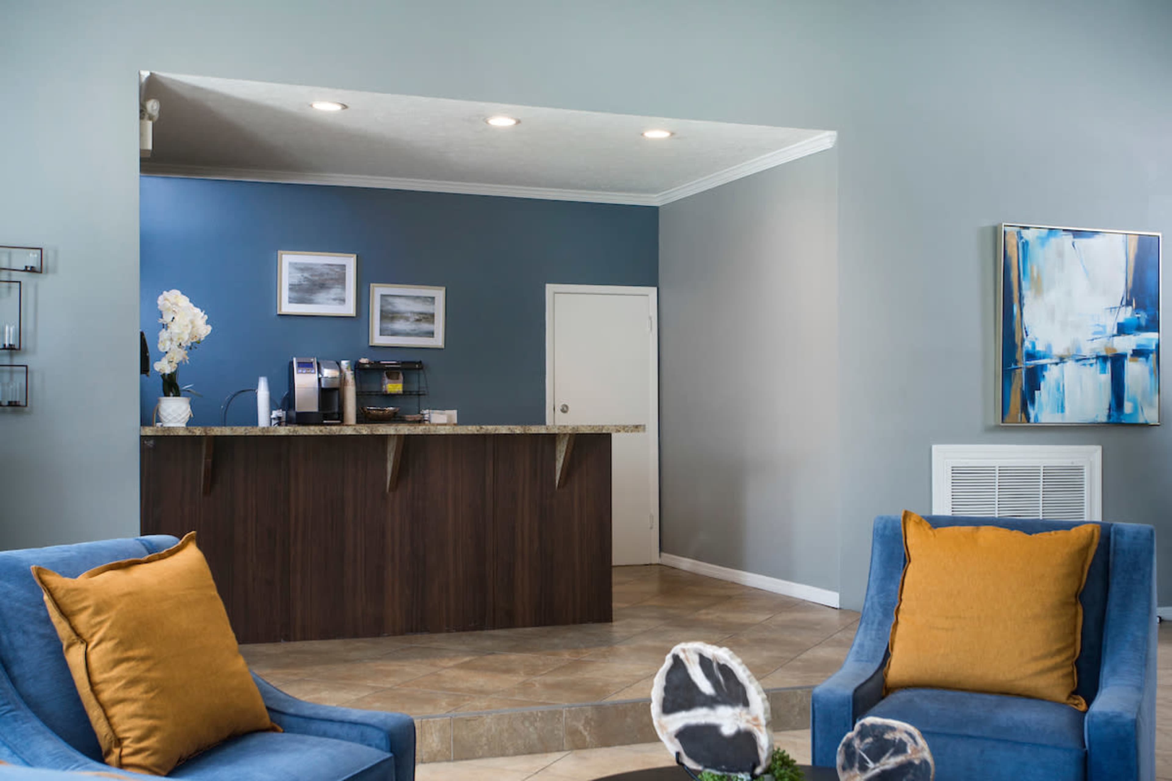 A modern reception area with a dark wooden front desk, blue-colored walls, and two blue upholstered chairs with orange cushions.