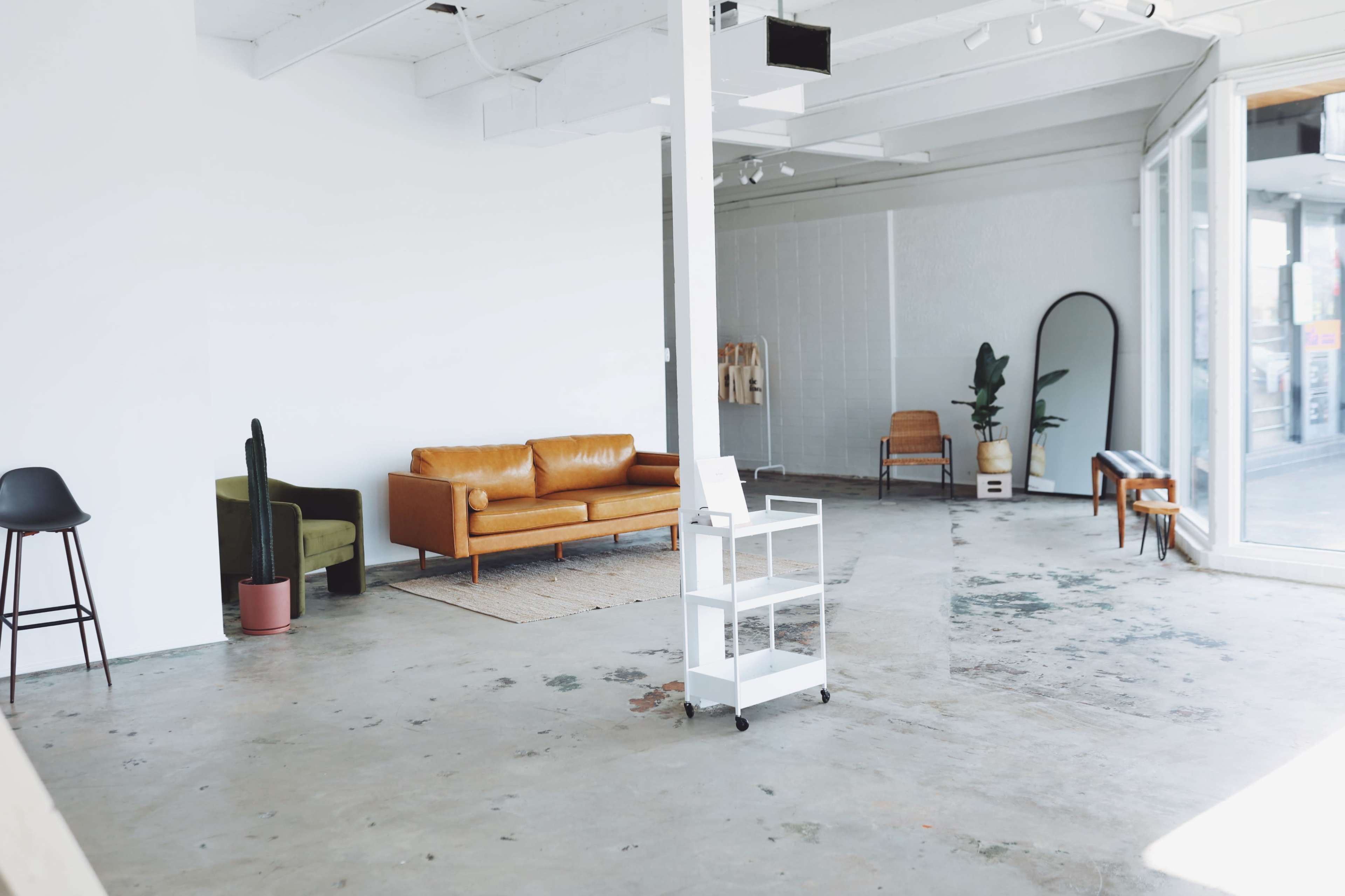 A spacious, minimally furnished interior with a leather couch, chairs, and a large mirror against a white wall.