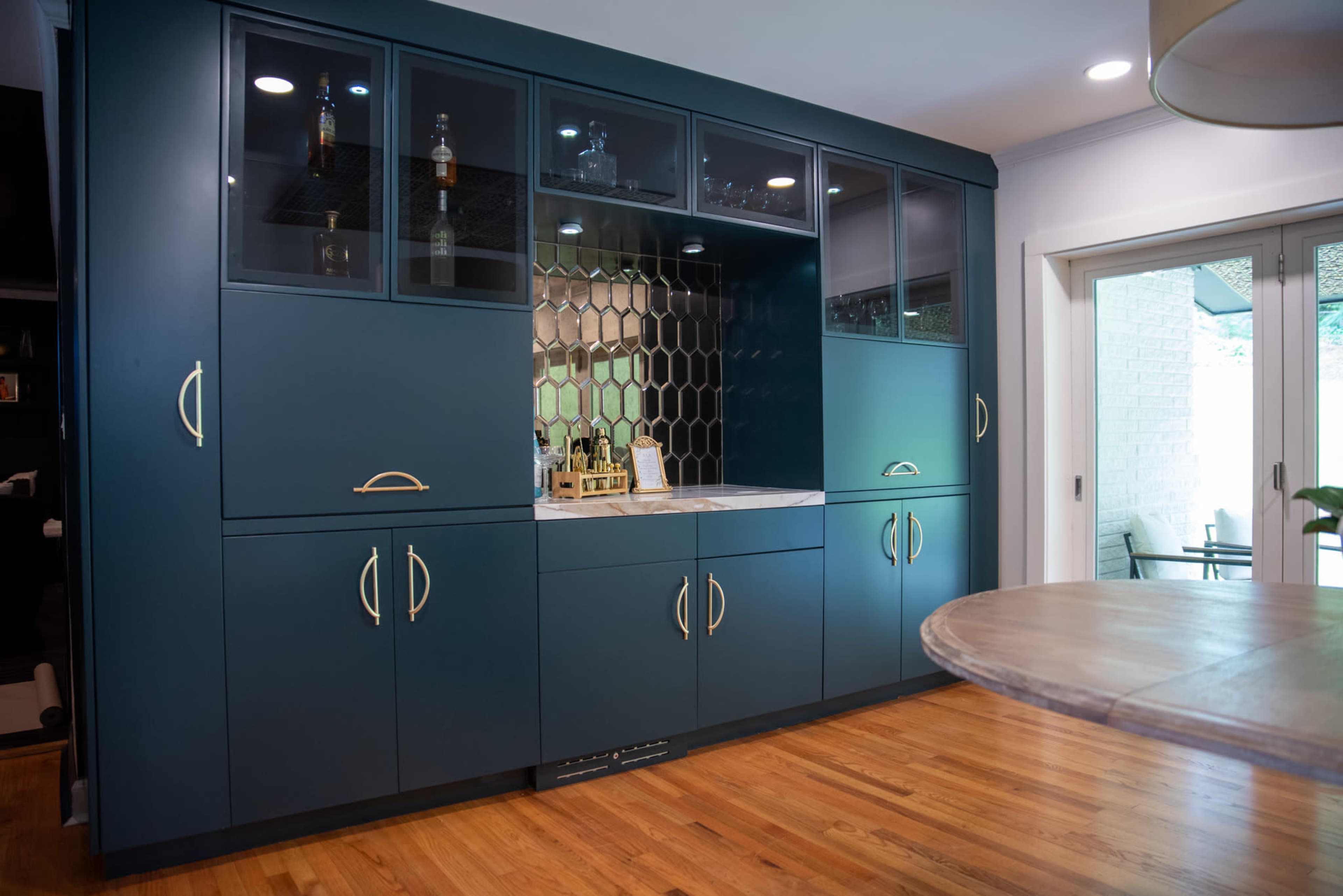 The image shows a modern kitchen area featuring a dark blue cabinetry with glass-front shelves and a hexagonal tile backsplash.